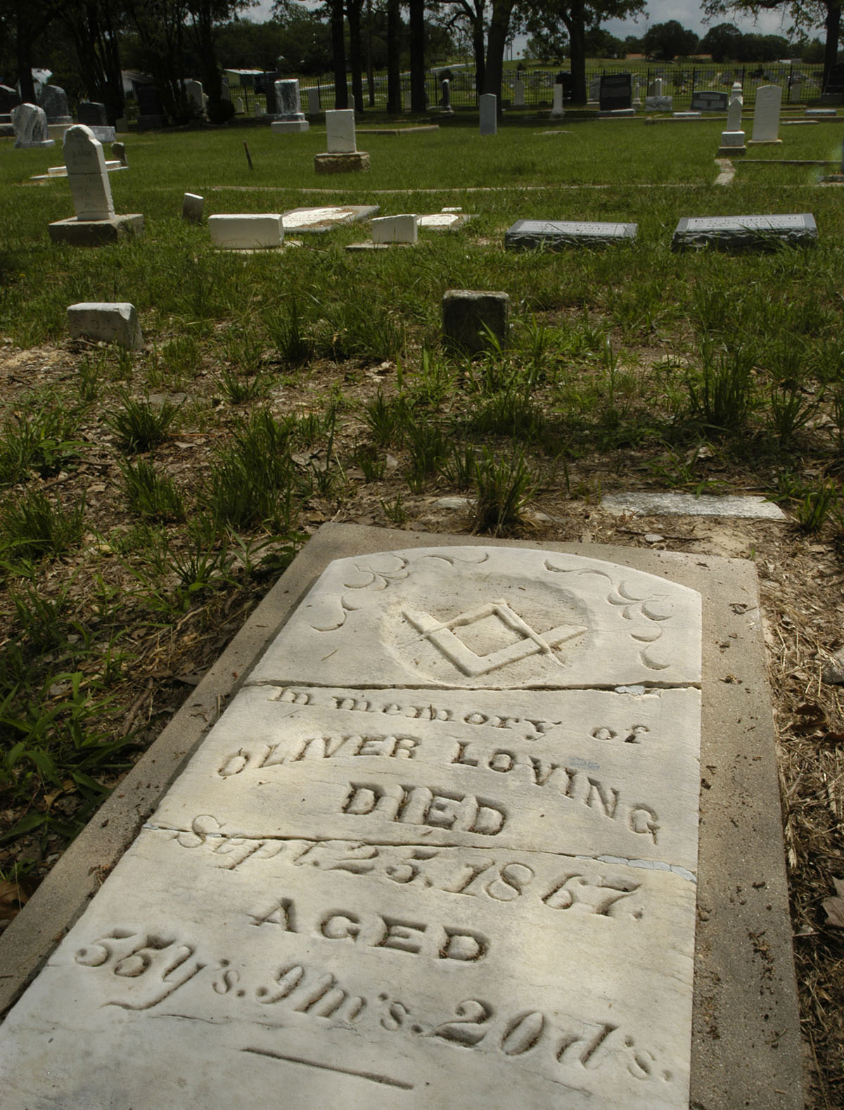 A cement gravestone reading "Oliver Loving Died Sept. 23, 1967" in a green cemetery
