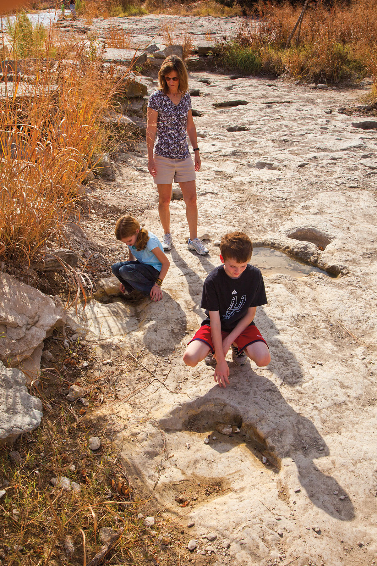 A woman and two children examine rock formations on a sunny way