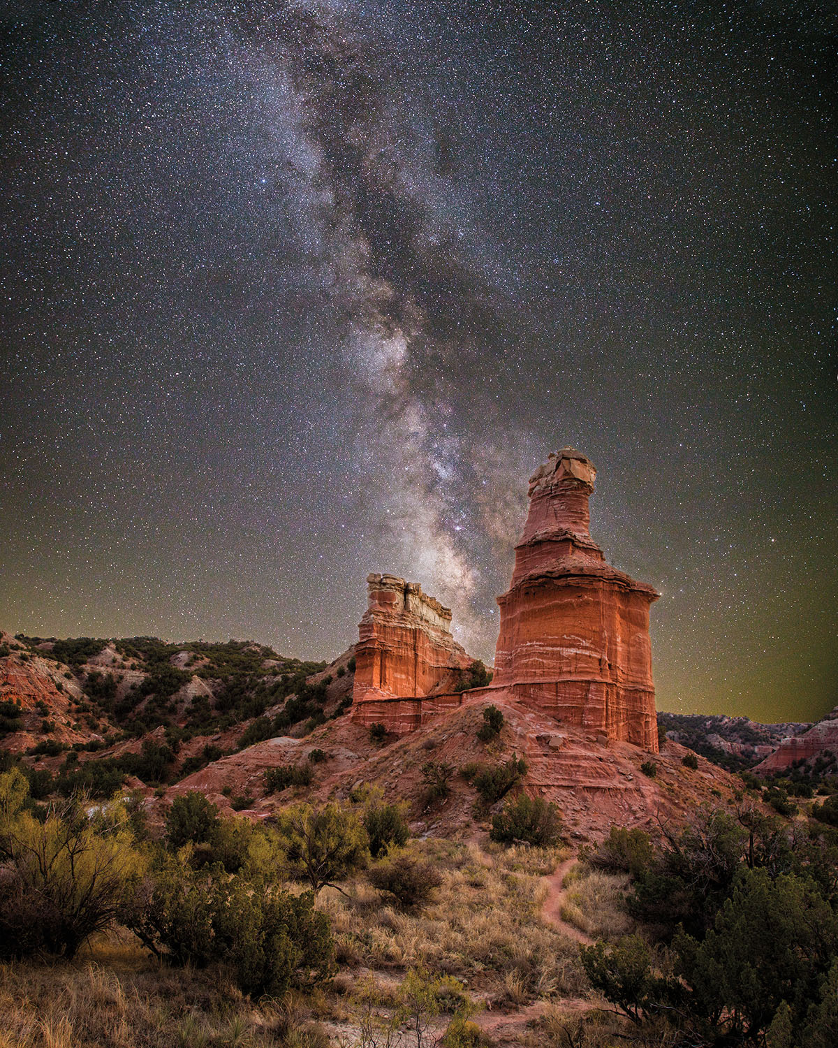 Bright red rock outcroppings in front of a dark sky scene of the Milky Way