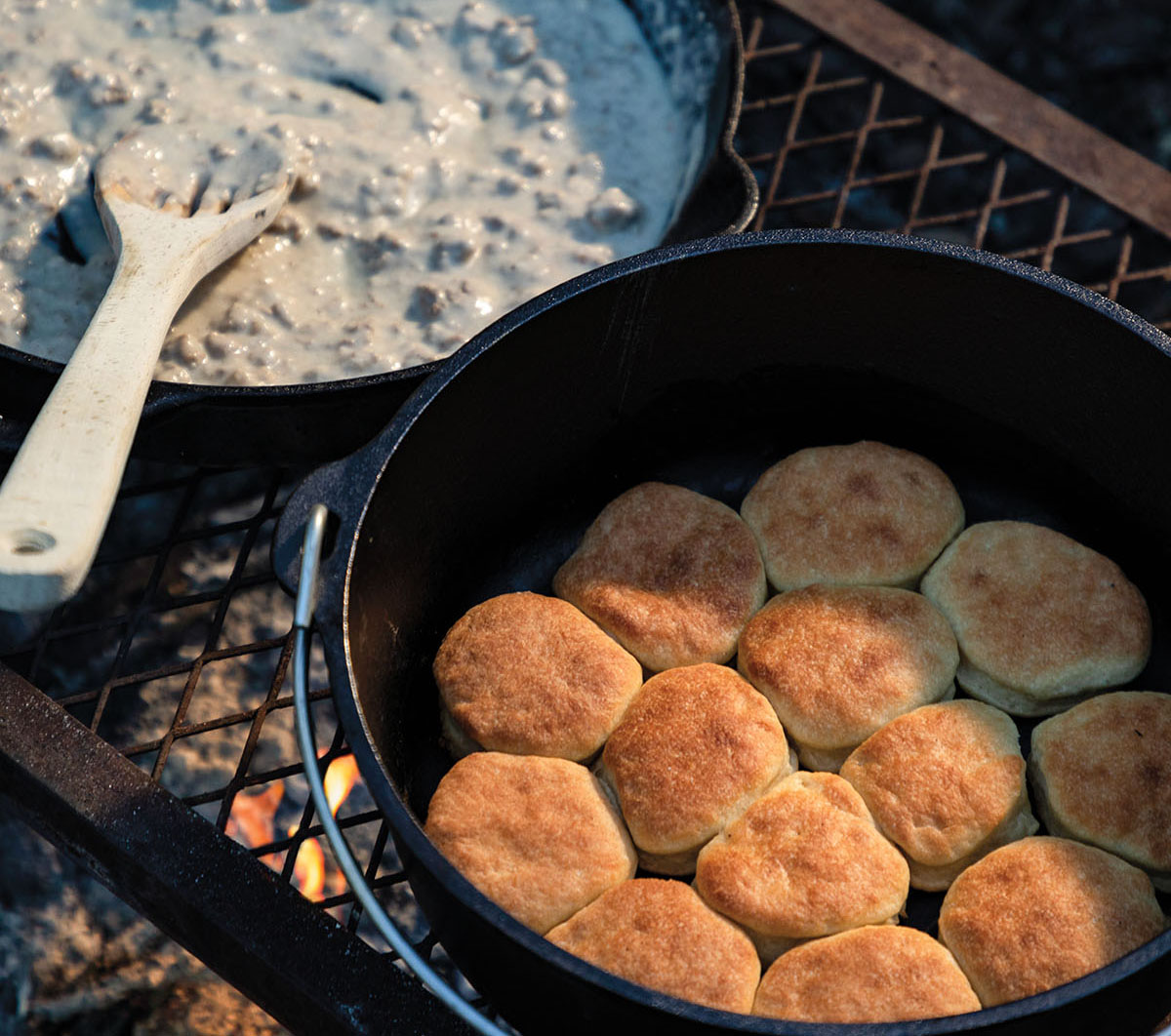 An overhead view of golden brown biscuits in a cast-iron dutch oven next to a large cast iron skilled filled with creamy gravy