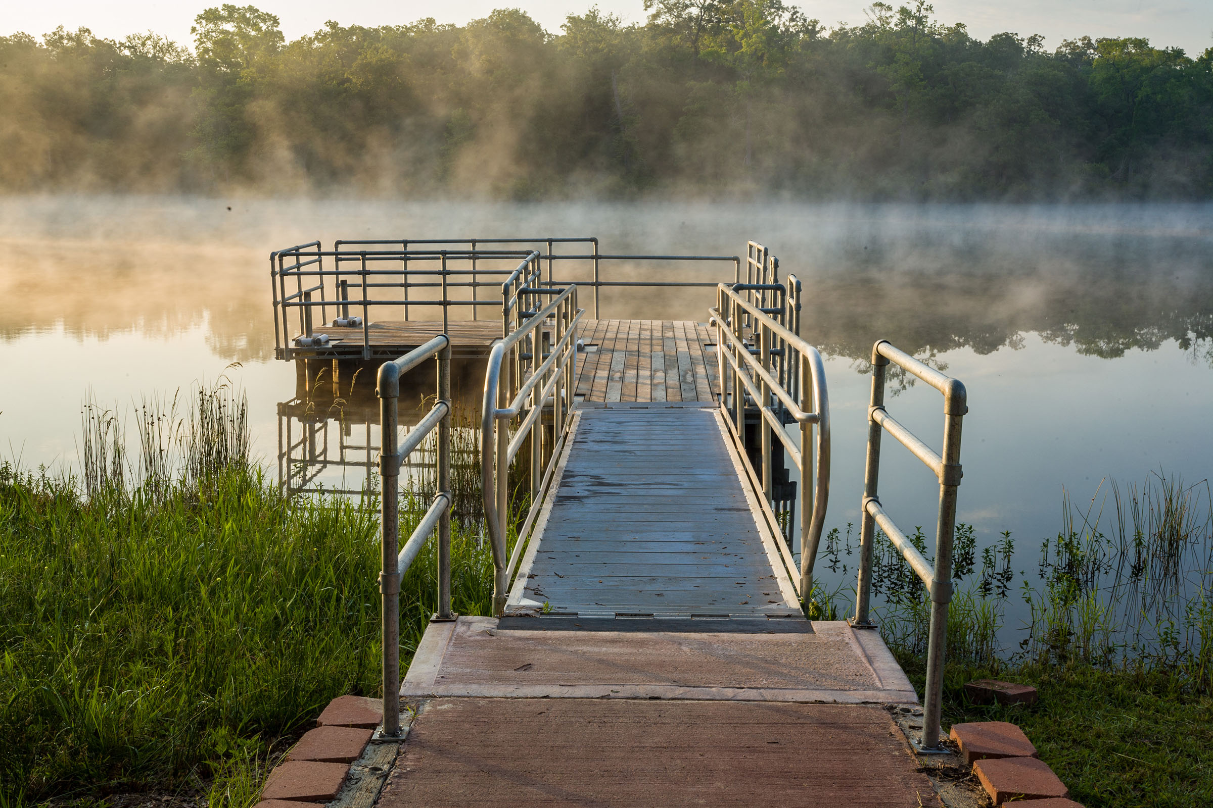 Steam rises off of a smooth body of water around a fishing pier