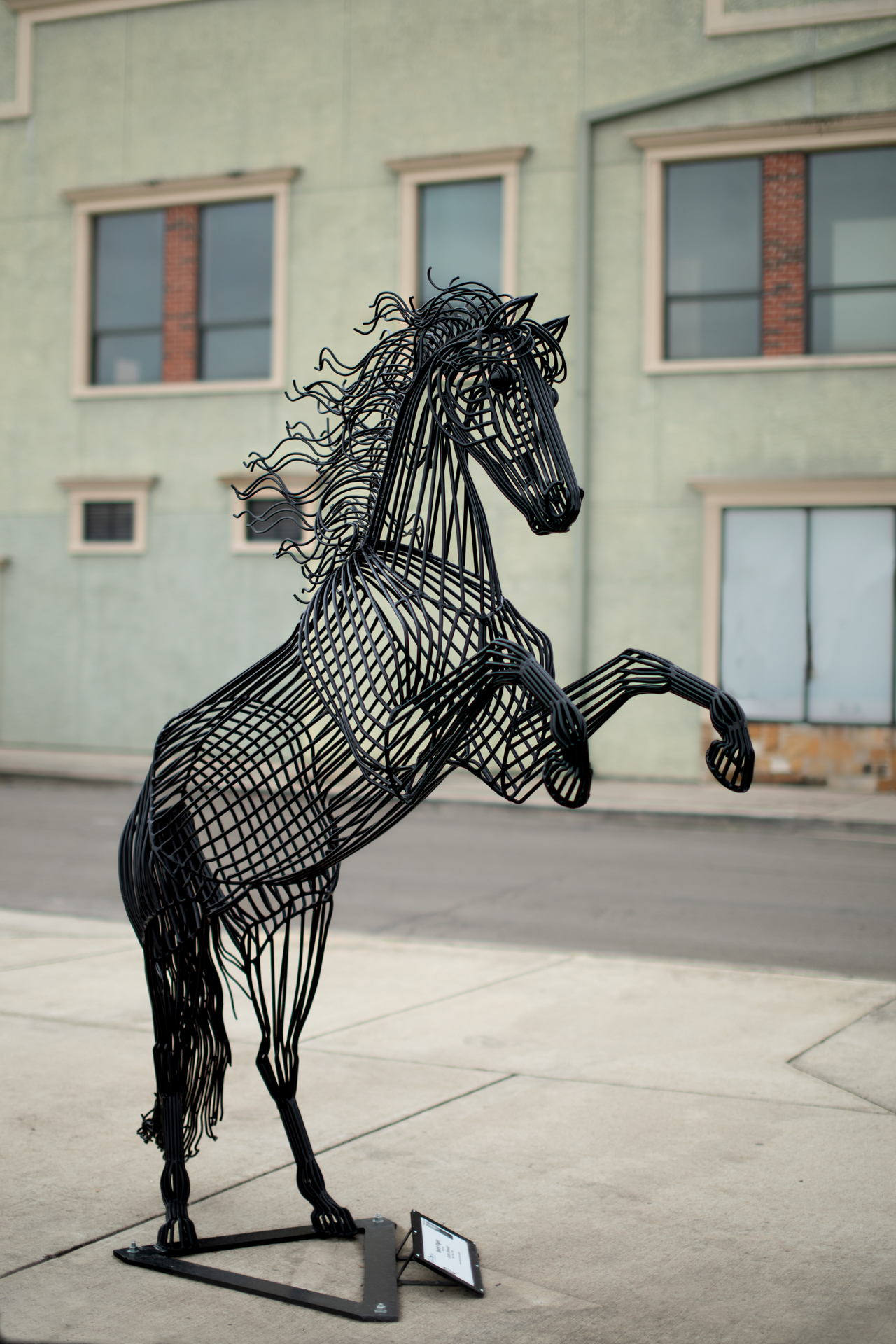 A metal sculpture of a black horse in front of a cream-colored building