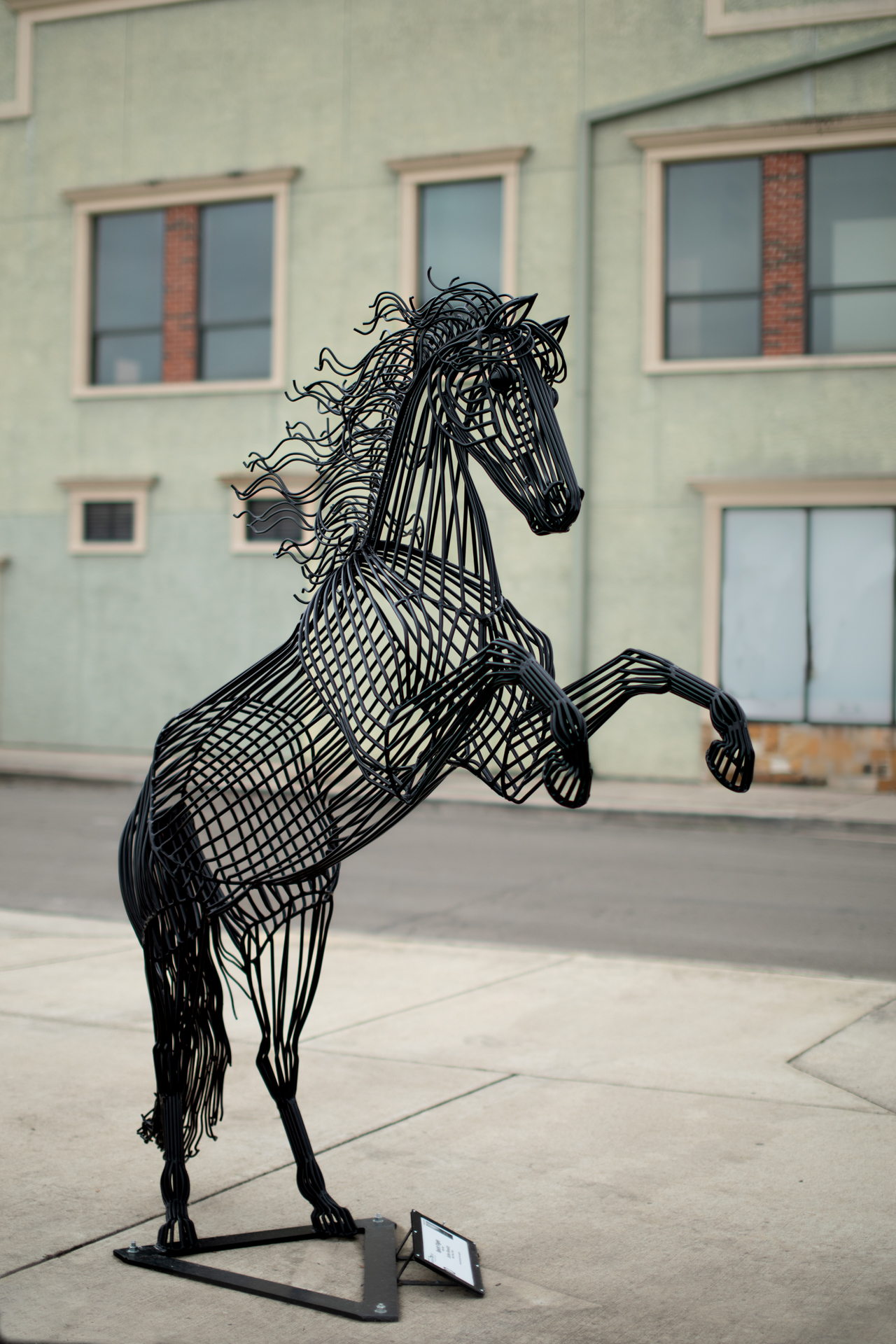 Unha escultura metálica dun cabalo negro diante dun edificio de cor crema