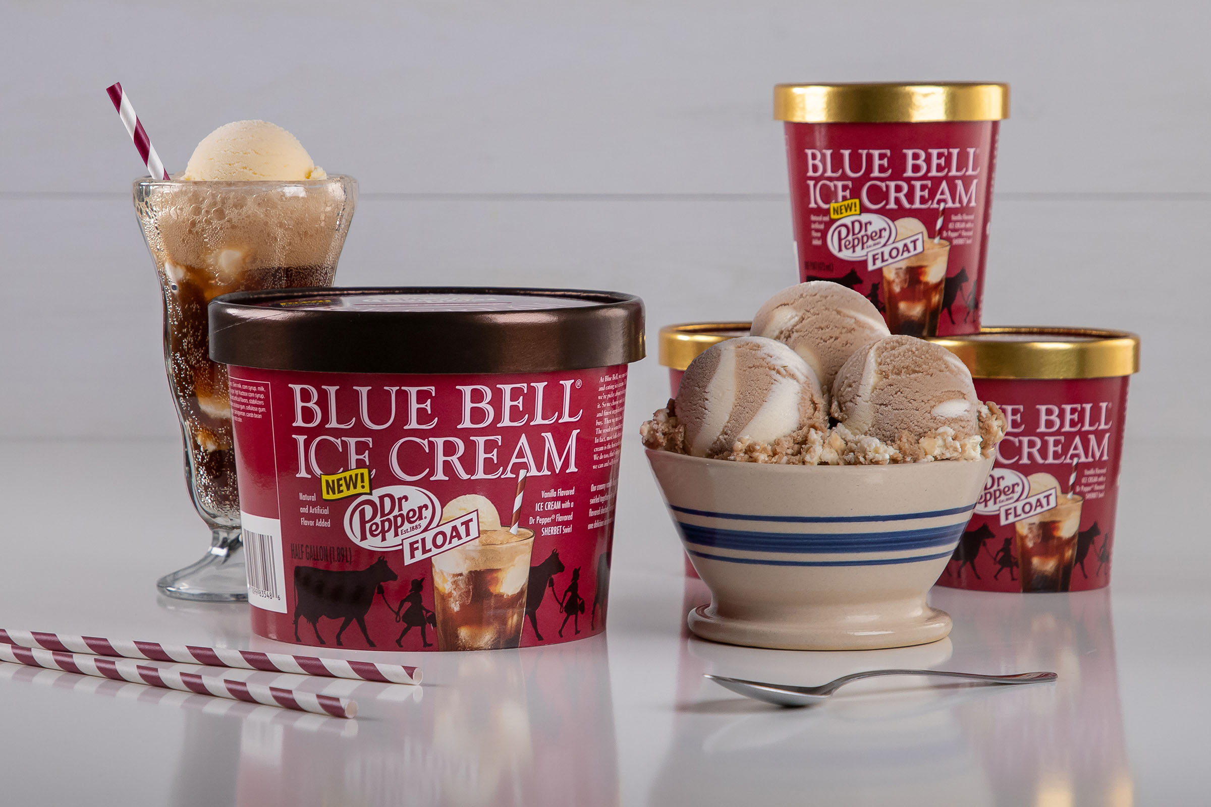 Containers of maroon Blue Bell ice cream and a ceramic bowl filled with scoops of Blue Bell