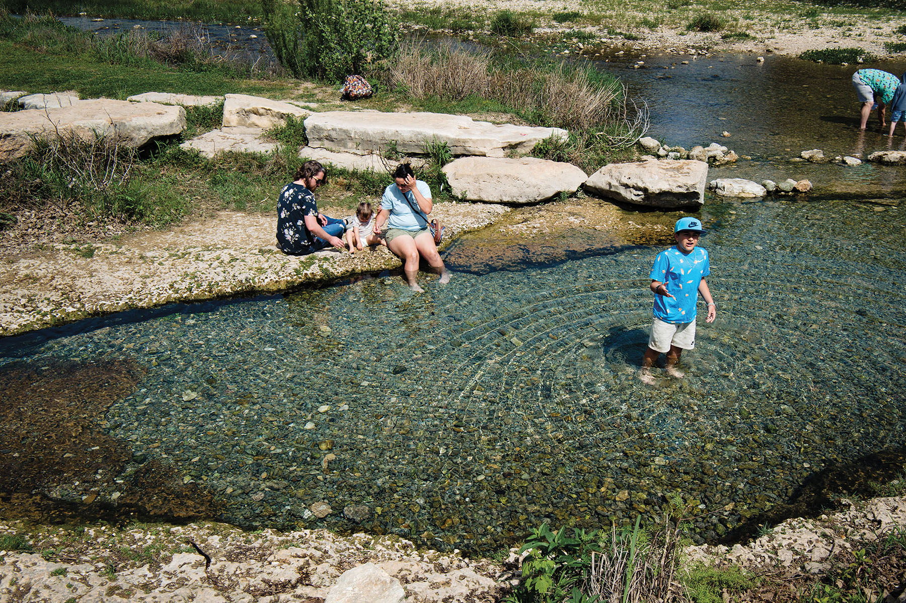 A group of people wade in green-blue water along a rock creek