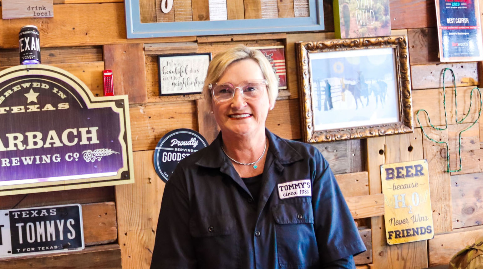 A woman stands next to several beer signs in a wood-paneled restaurant