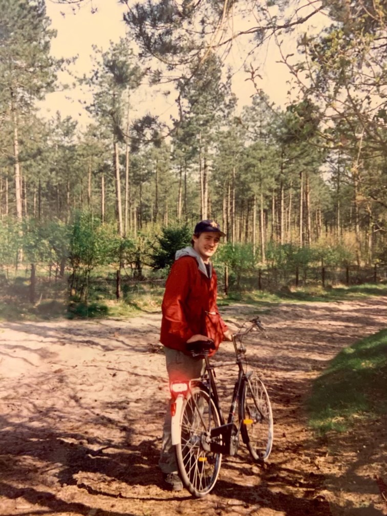 A man stands with a bicycle in a wooded area