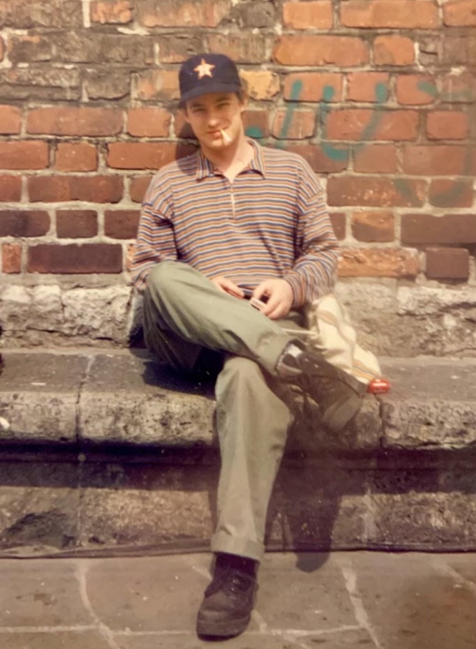 A man in a striped shirt and Houston Astros hat sits on a rock wall