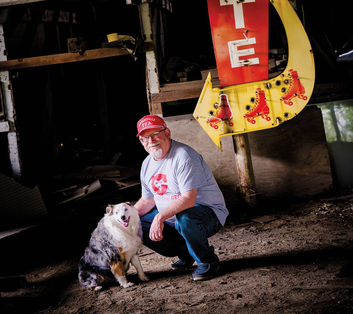A man leans down to pet a dog beneath a bright yellow and red sign with arrows