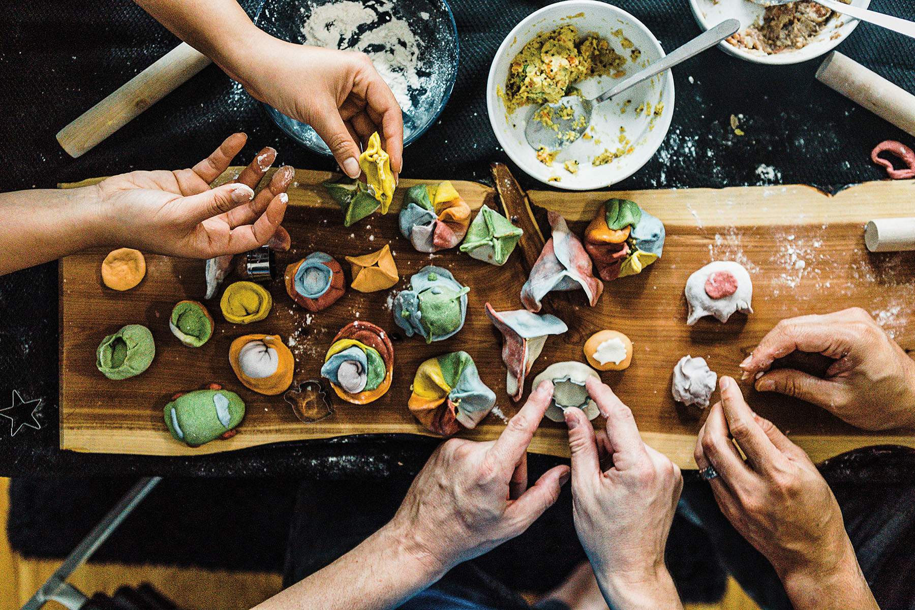 An overhead view of people folding colorful dumplings on a wooden work table