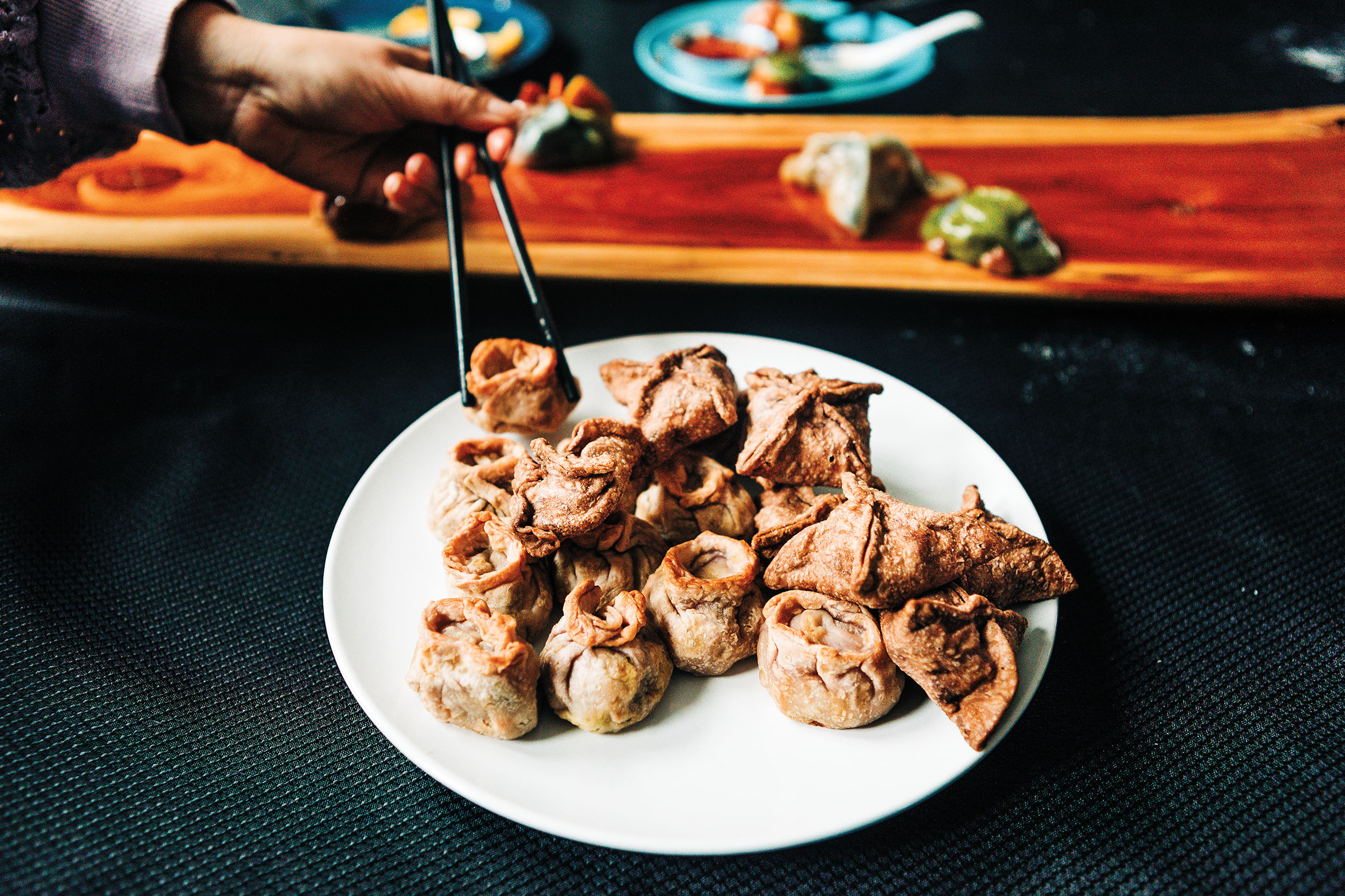 A person uses chopsticks to pick up a golden fried dumpling on a white plate