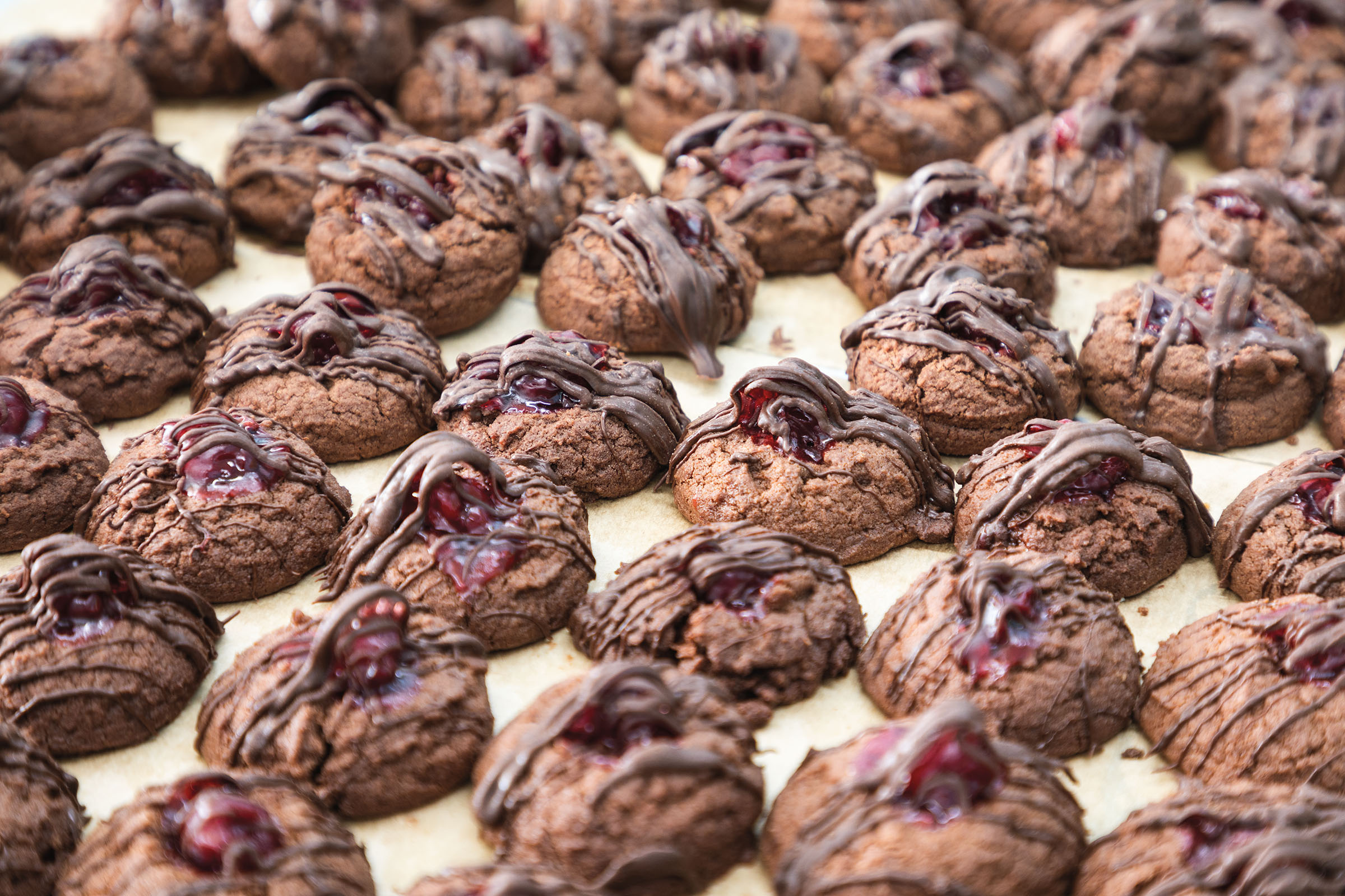 Several dozen chocolate cookies with a small red cherry and chocolate drizzle