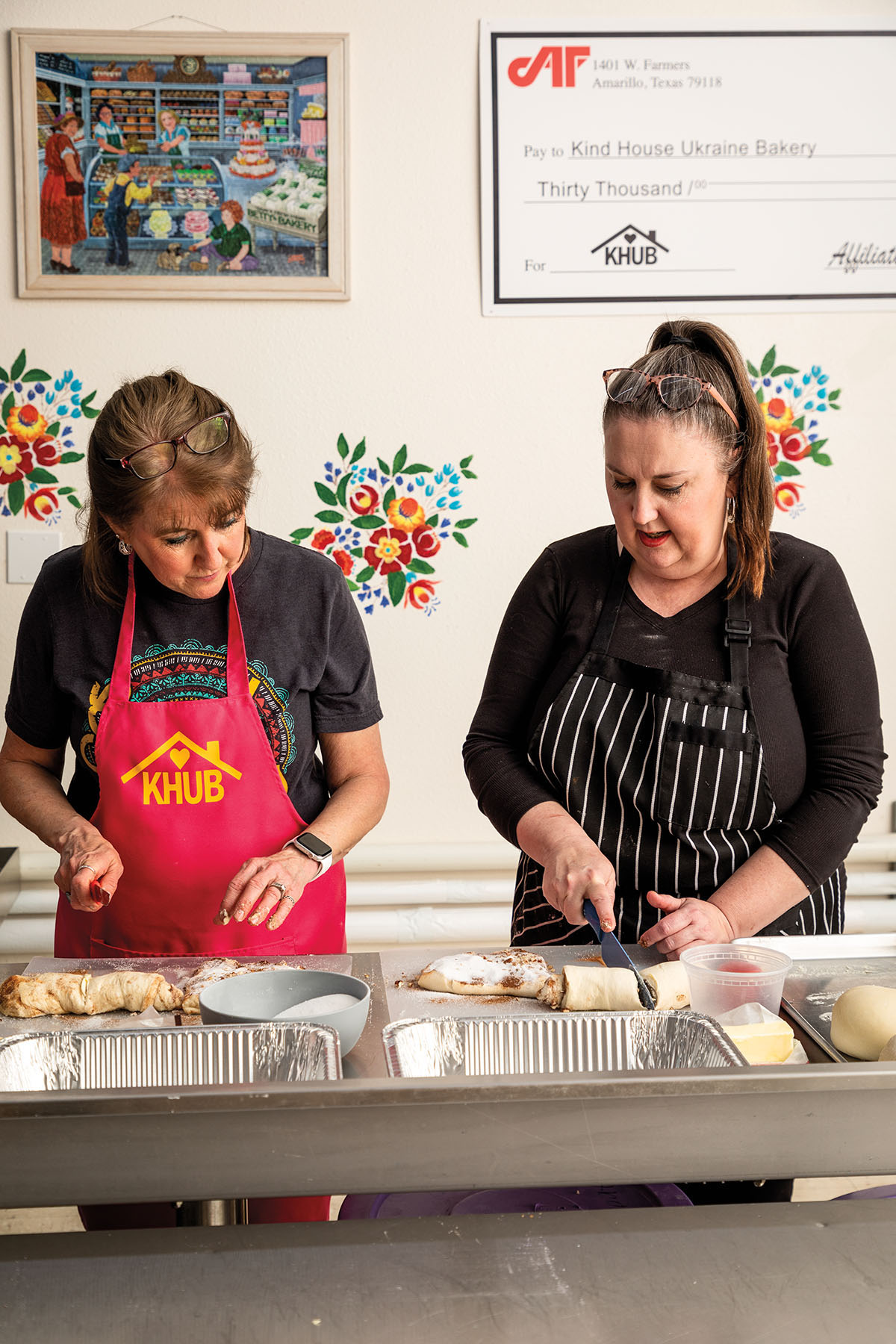 Two women in aprons work with dough and bowls of sugar on a work surface