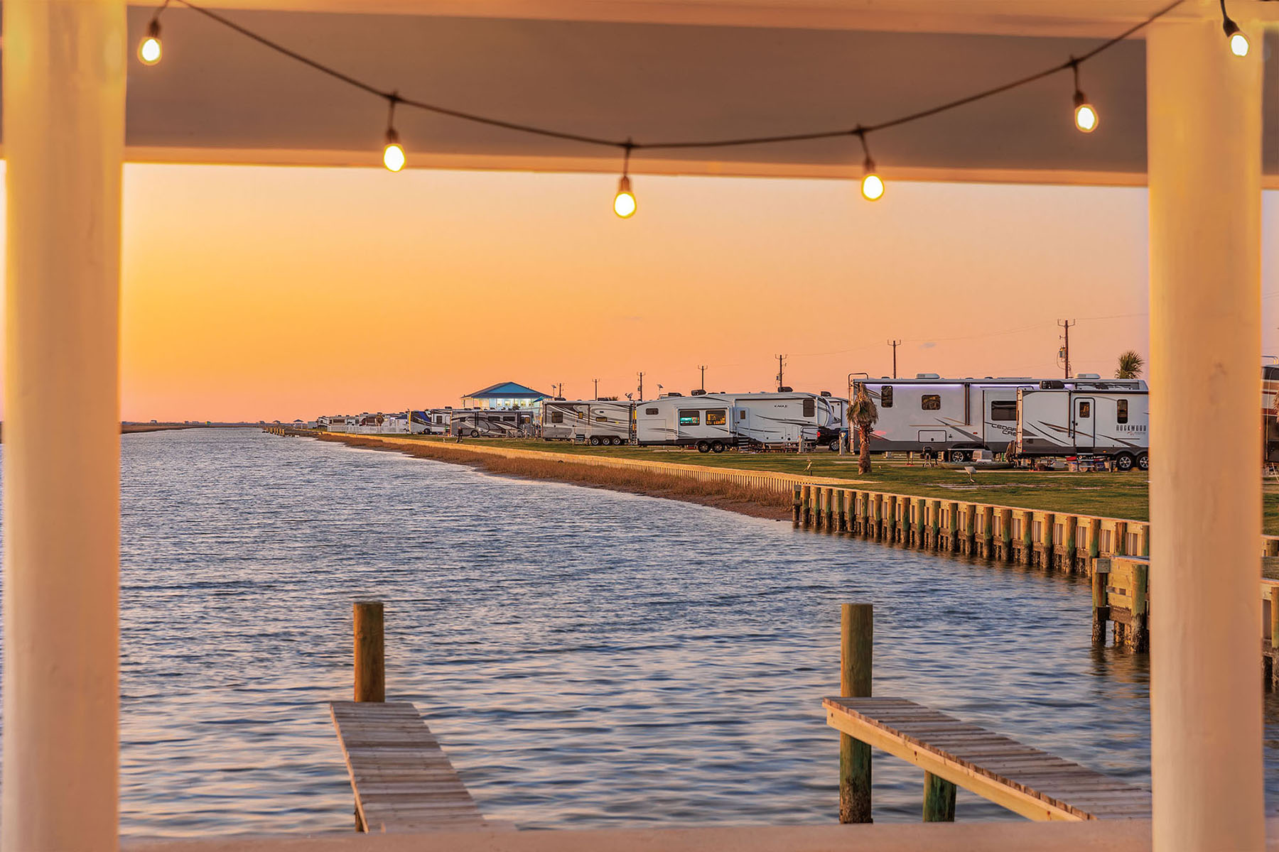 The view down a wooden pier with string lights and an orange-pink sunset