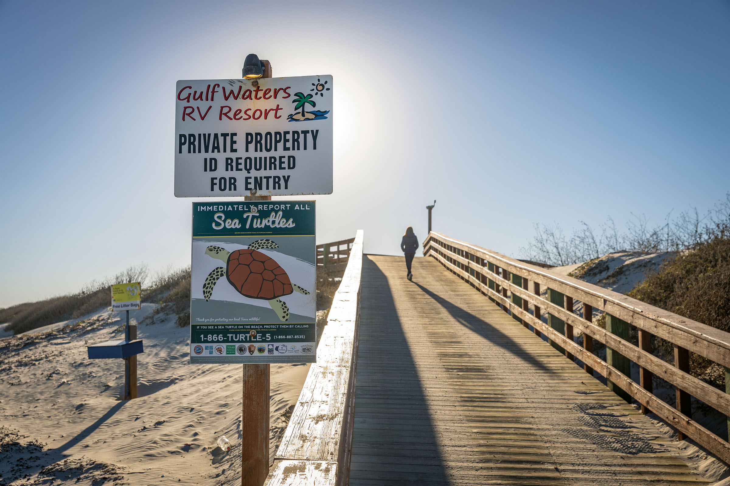 A sign next to a boardwalk reading "Private Property - ID Required for Entry" and another reading "Immediately report all sea turtles"