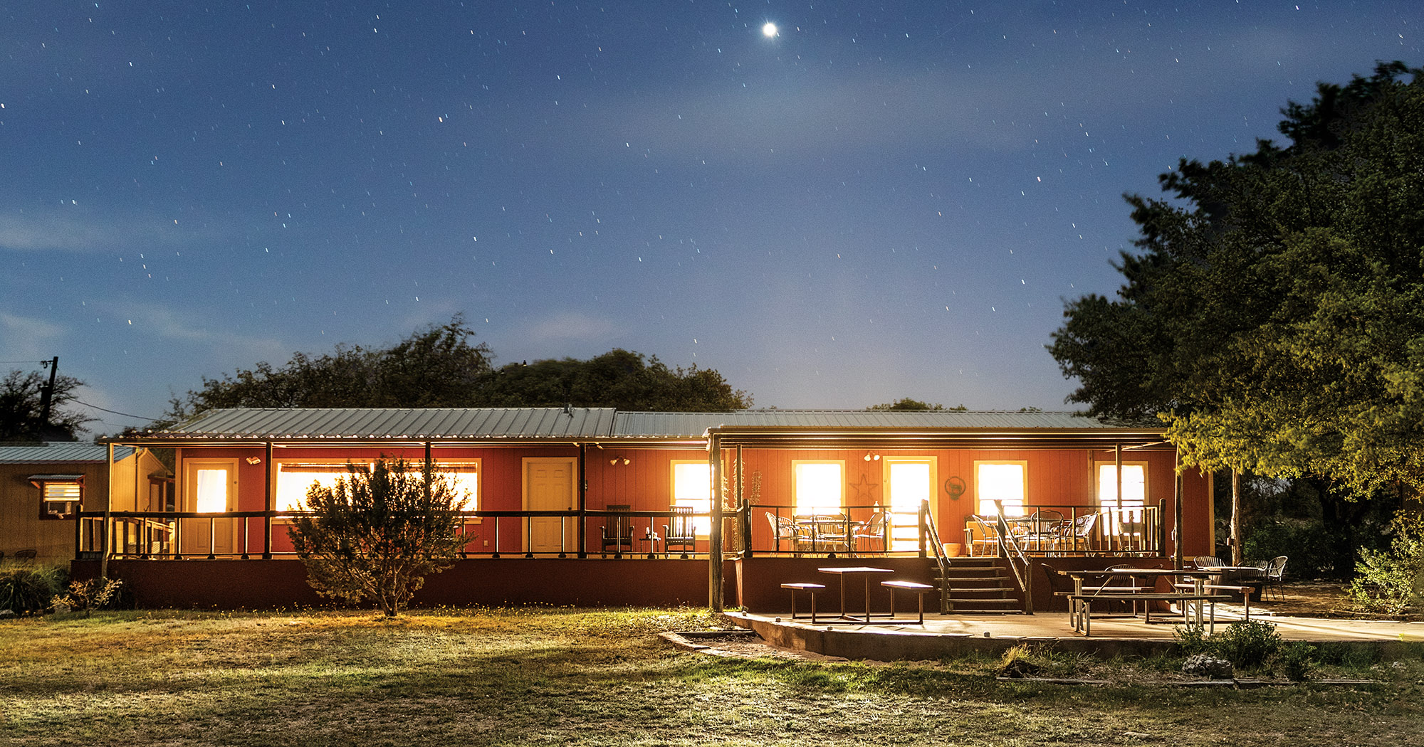 The exterior of a lodge glows with bright lights in the night under a blue starry sky