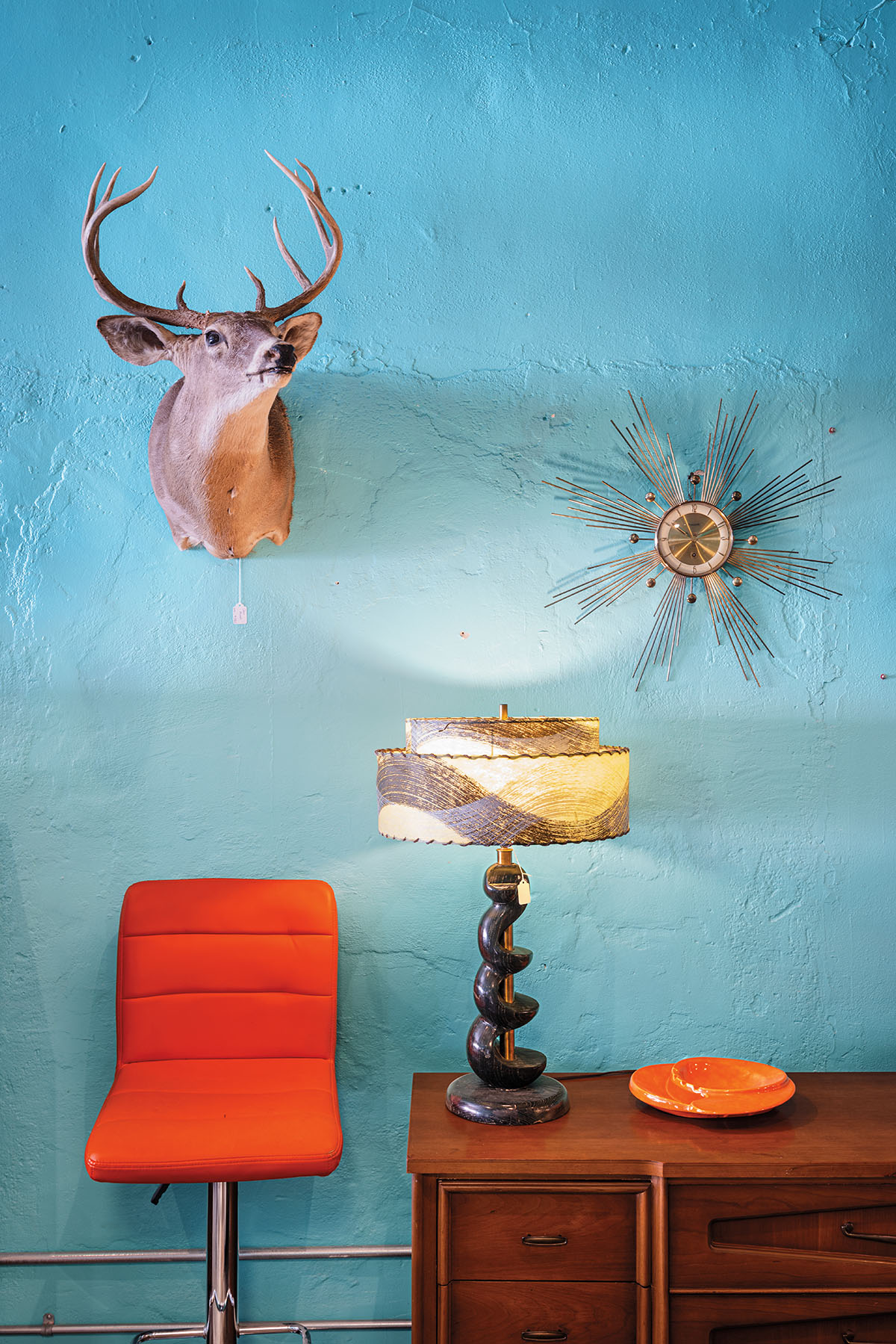 Taxedermined animals and wall art adorn a bright blue wall with a red chair