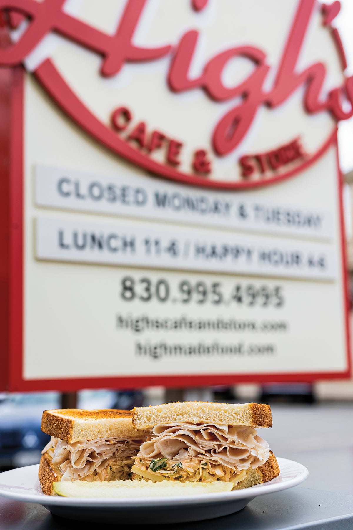 A sandwich piled high with meat in front of a sign reading "High's Cafe and Store"