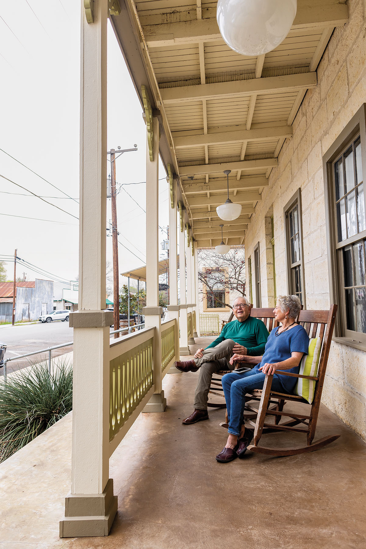 Two people sit in rocking chairs on a porch in a small town