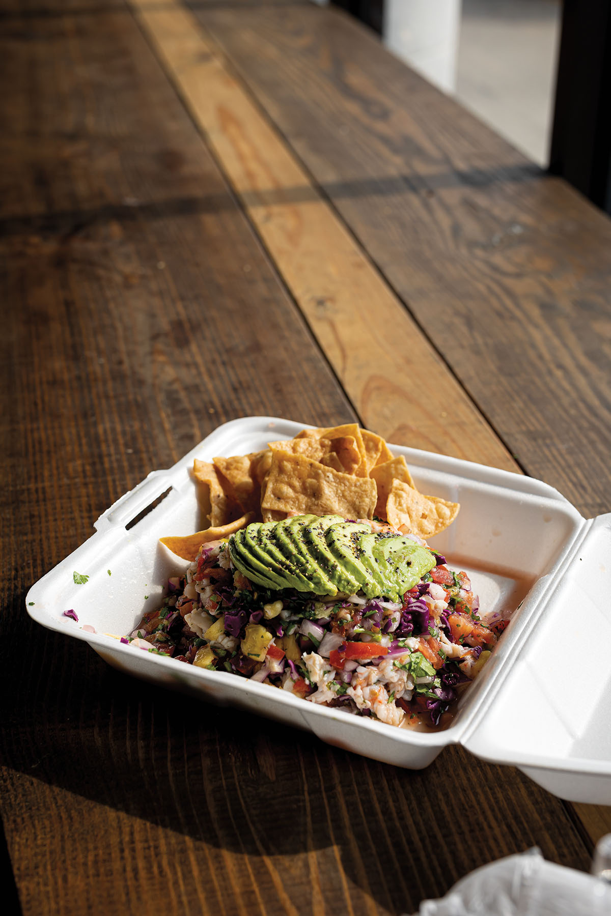 A takeout box filled with a large portion of ceviche complete with toasted tortilla chips