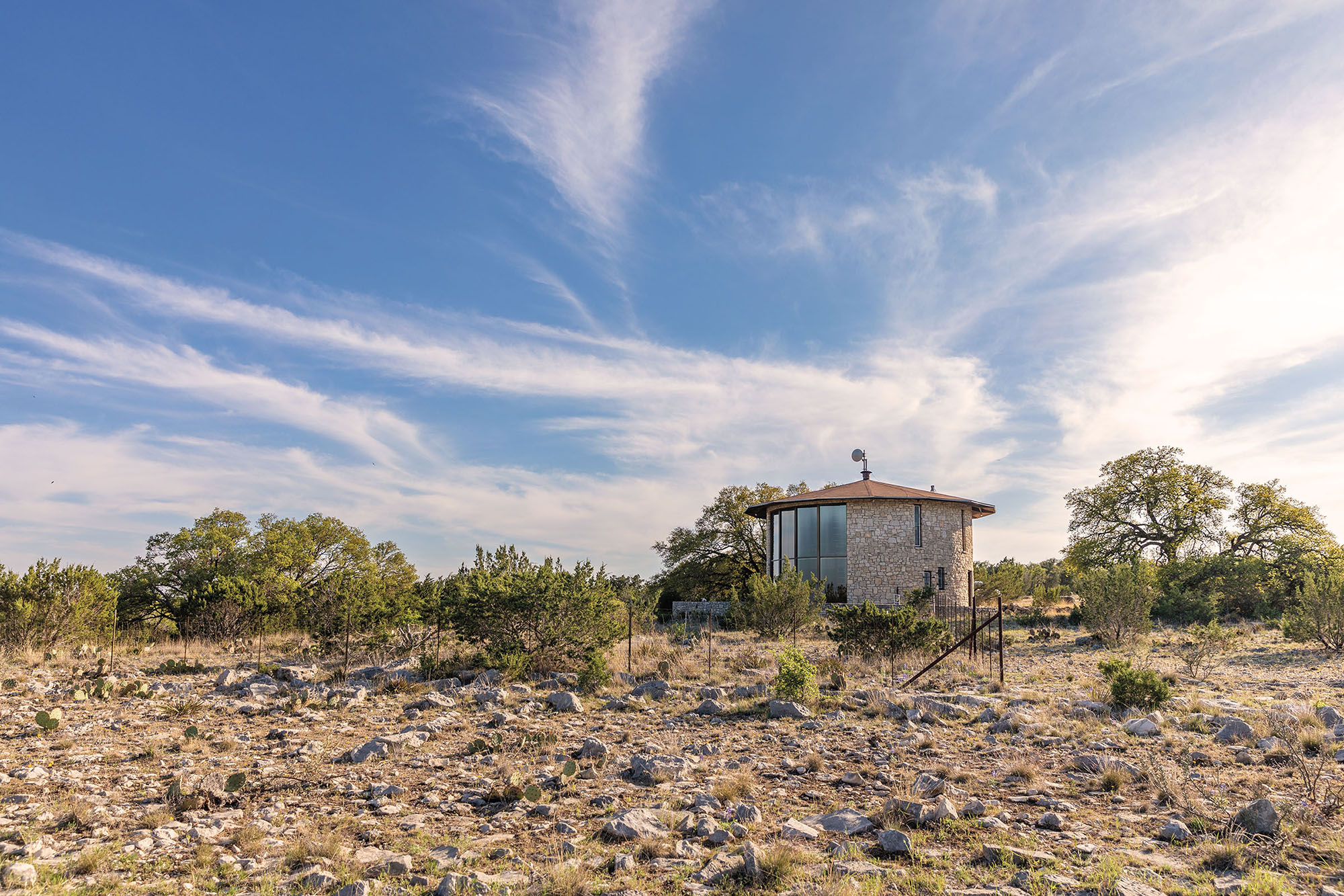 A small stone building on a large rocky landscape with green trees under blue sky