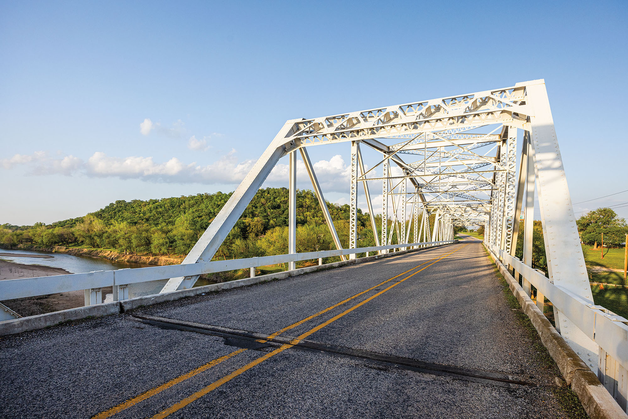 A white bridge with a roadway across clear blue water and green hills