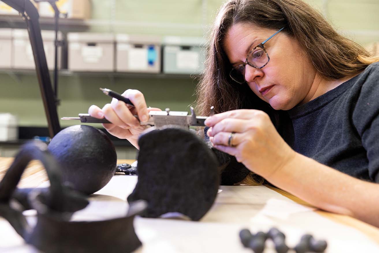 A women measures a piece of an artifact.