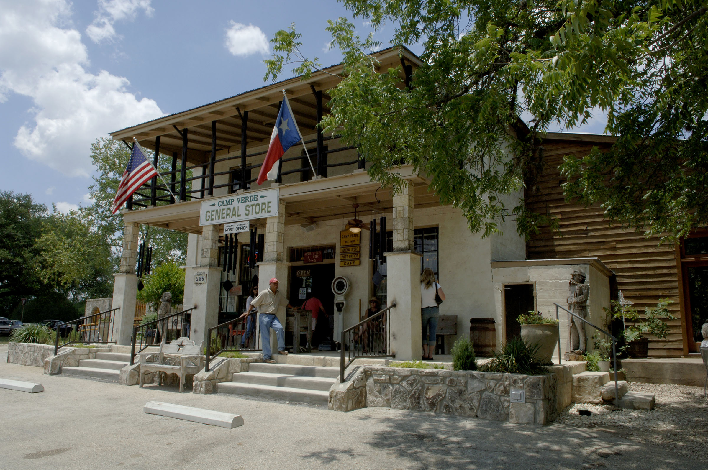 The exterior of a large general store, with stonework halfway up large wooden pillars and a sign reading "Camp Verde General Store"