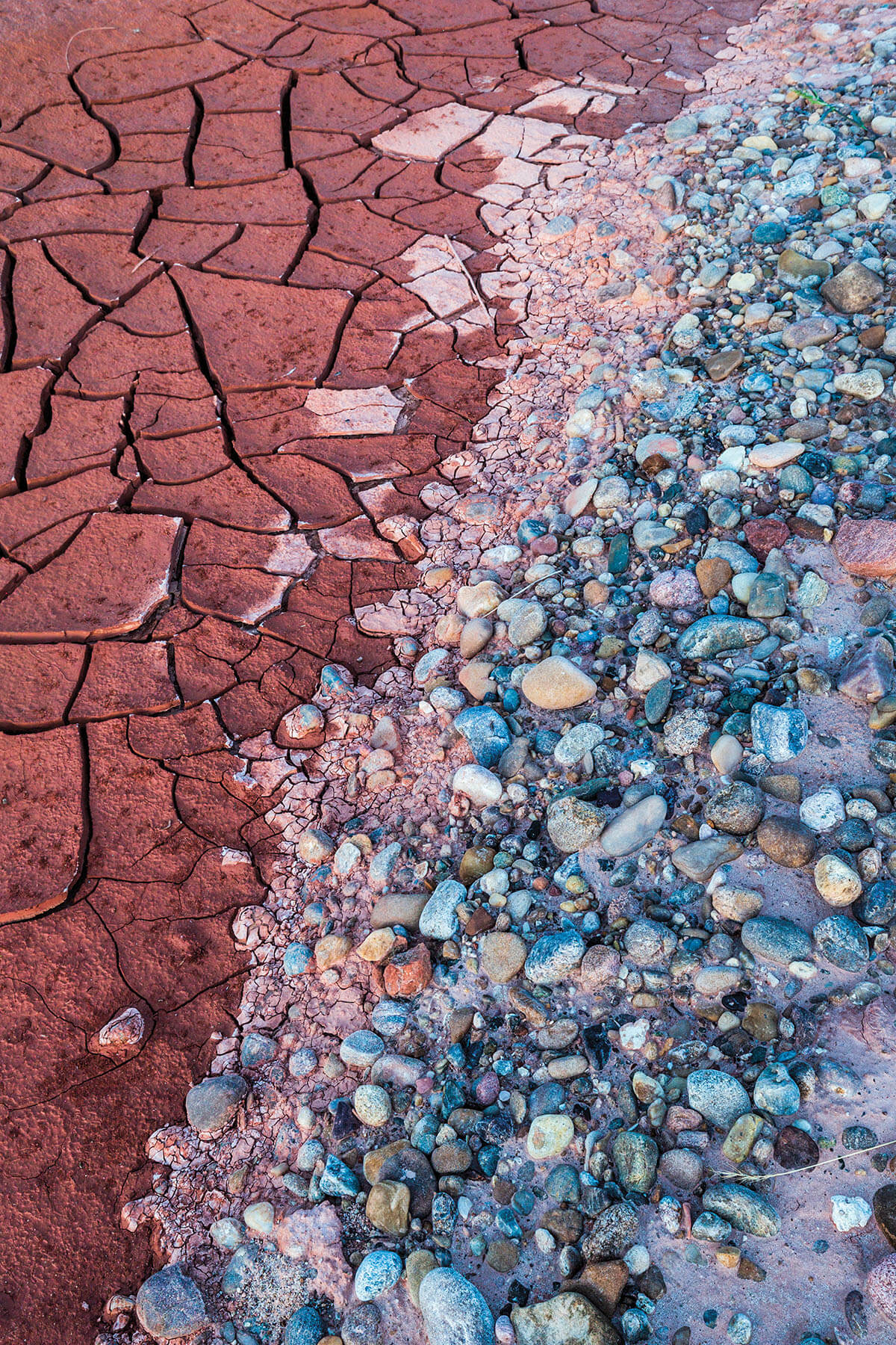 Dark red, cracked mud meets shiny blue water along the banks of a river