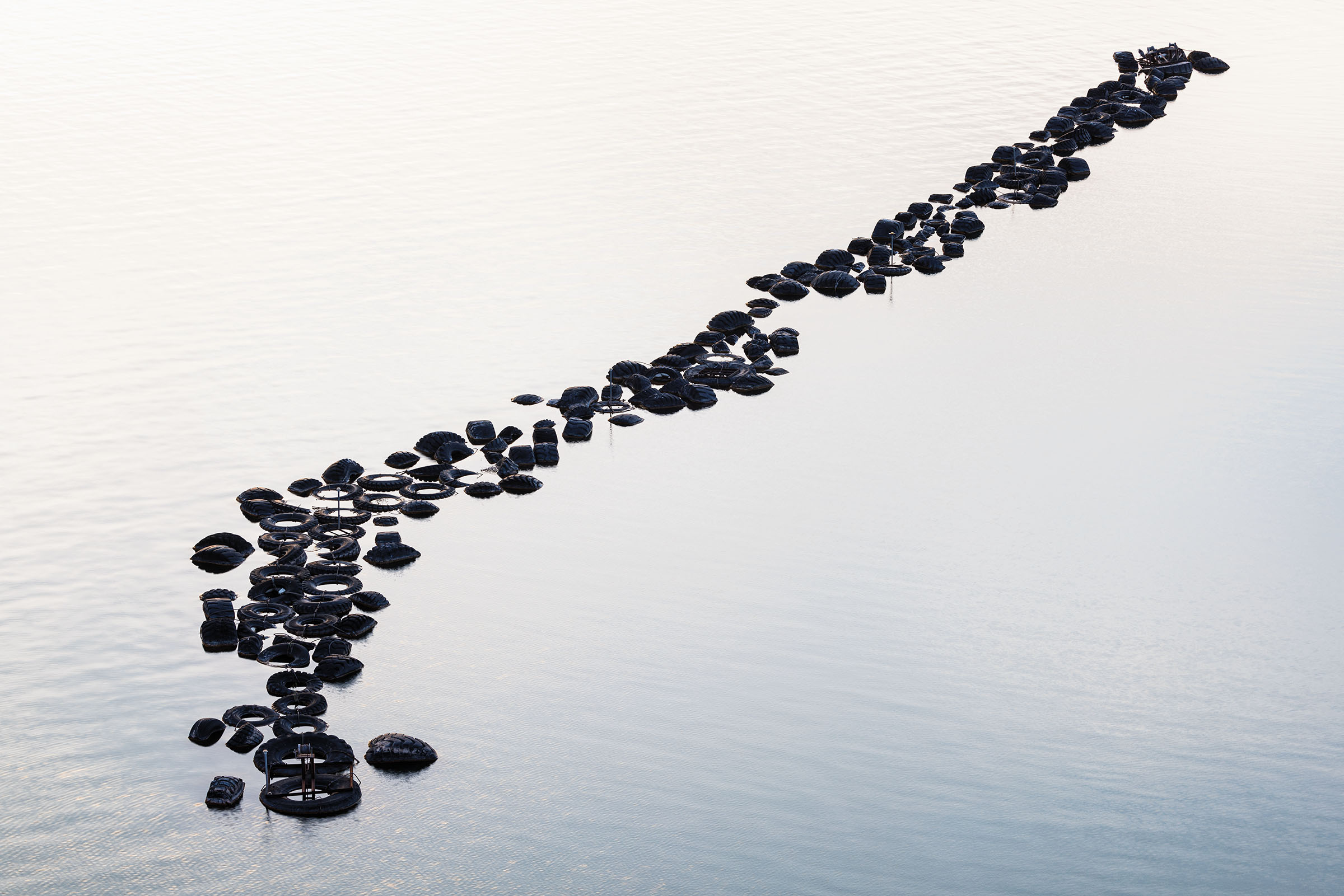 A group of dark tires form a long line in flat gray water