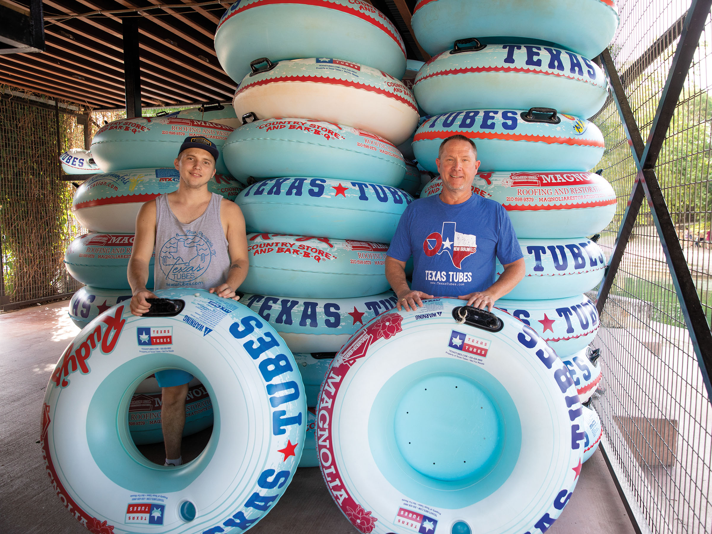 Two people stand holding tubes in front of a large stack of turquoise, blue and white river tubes
