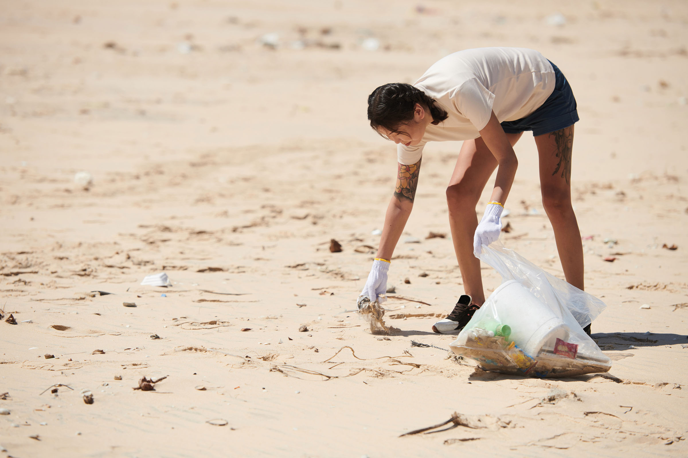 Young woman wearing textile gloves when picking up trash on sandy beach on Earth day