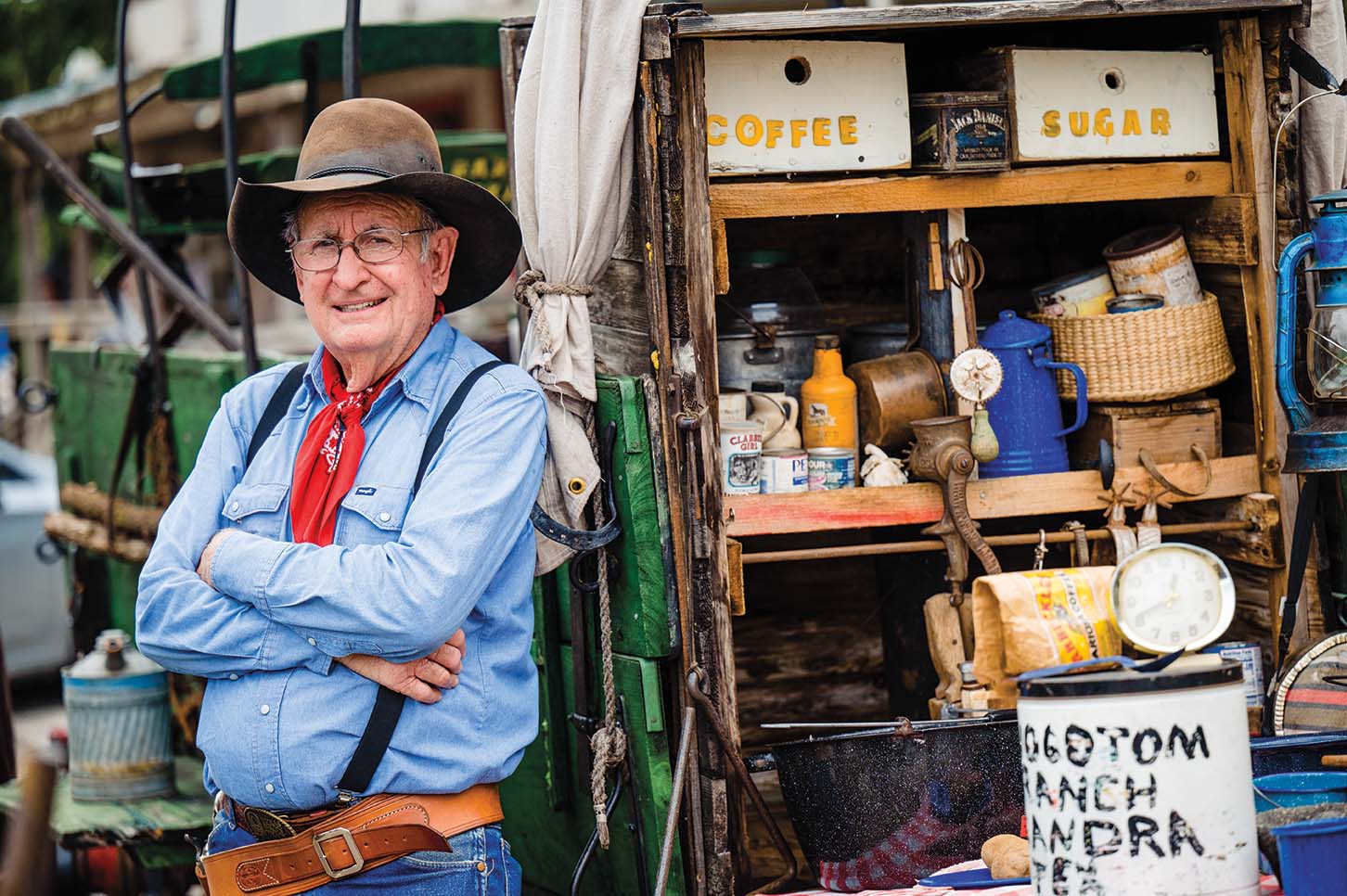 An older man standing with his arms crossed by a cabinet filled with knickknacks