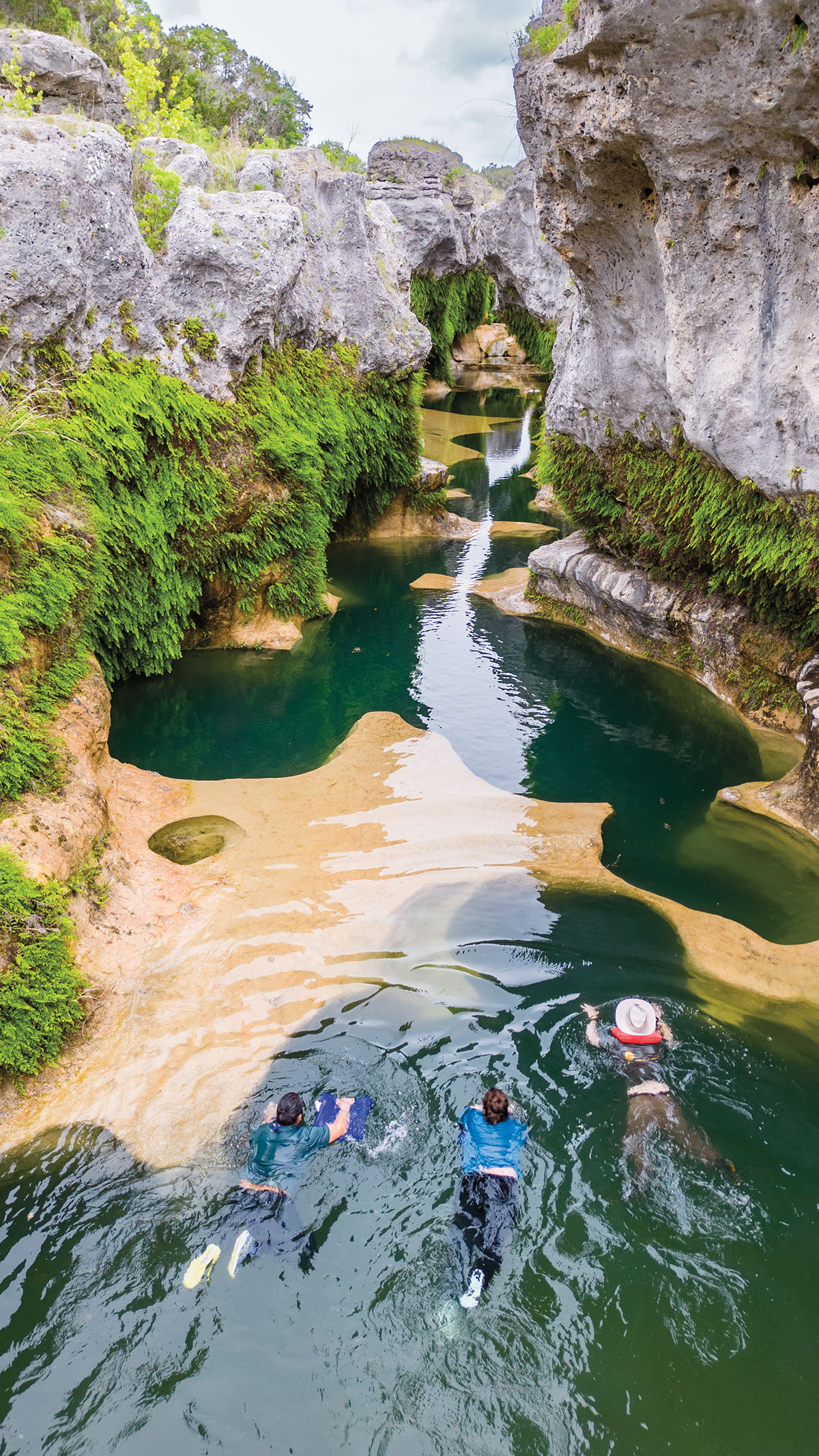 A group of people swim in small dark blue pools between large gray rocks