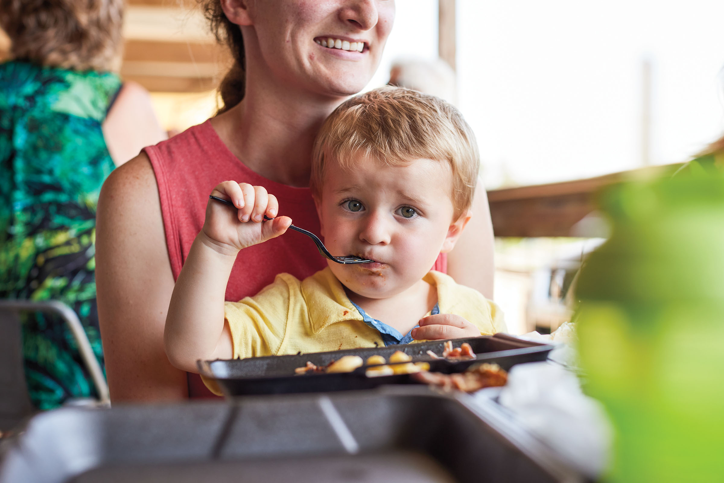 A child holds a spoon in his mouth in front of a dish of food
