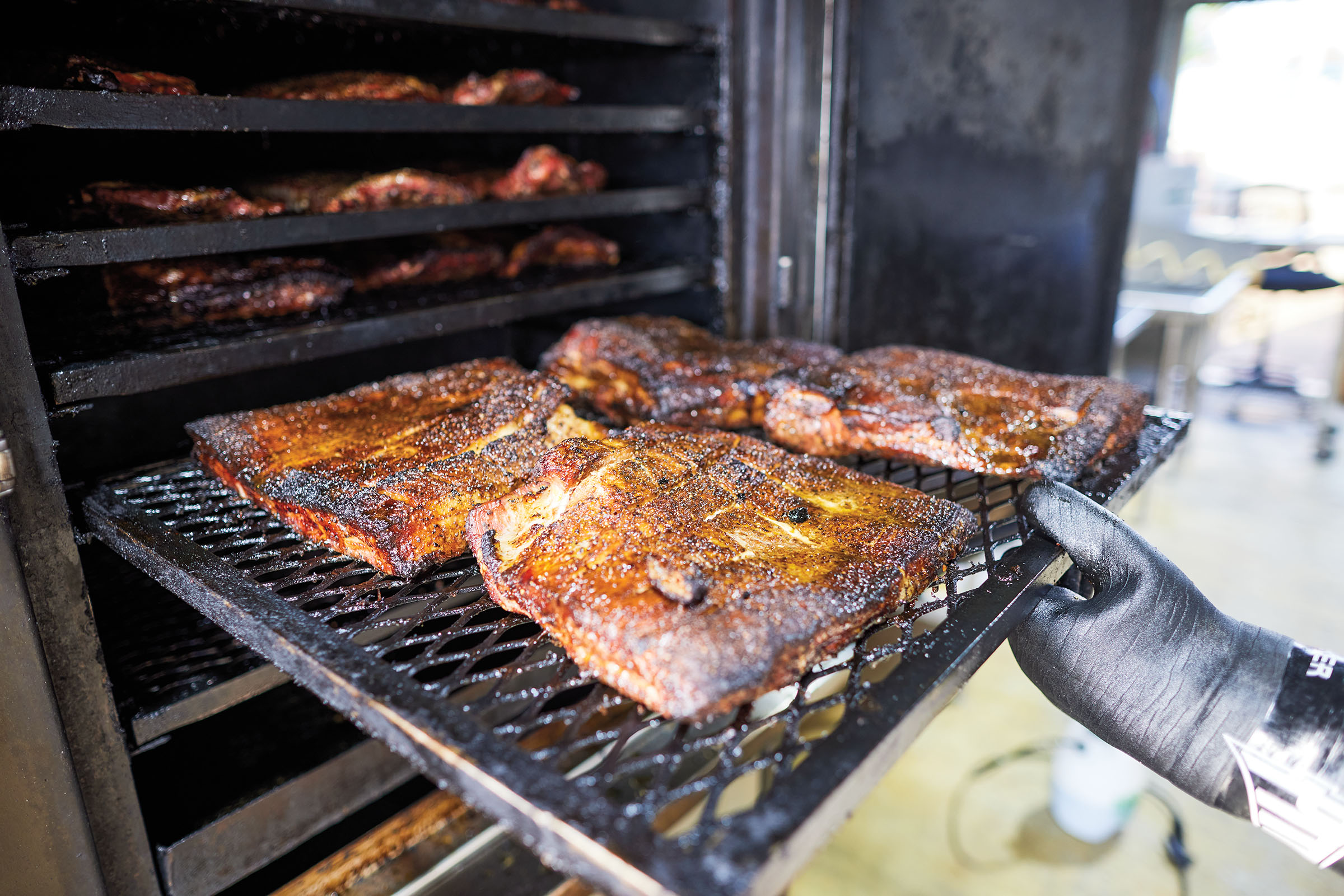 Four slabs of meat are loaded onto a metal tray and placed into a smoker
