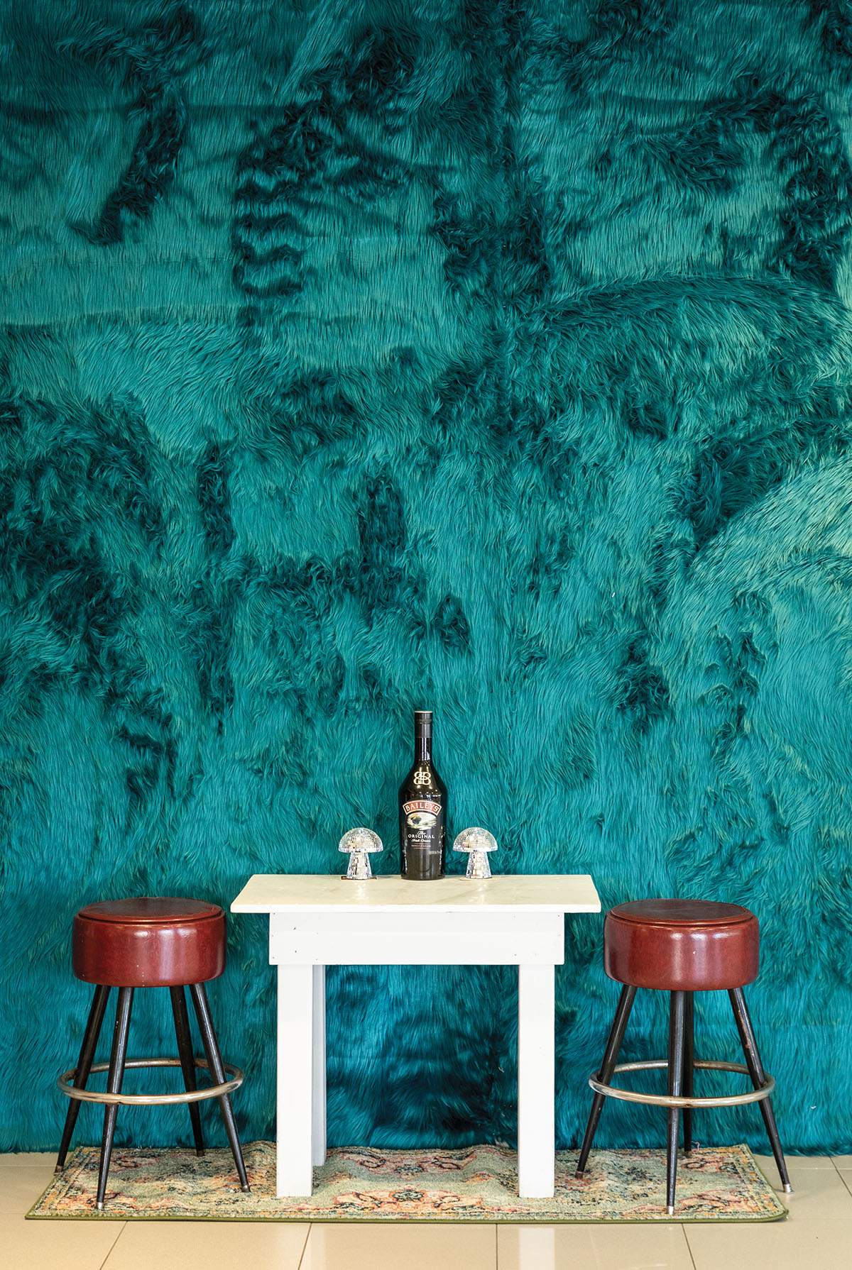 Two red barstools next to a white table in front of a wall decorated with turquoise fur