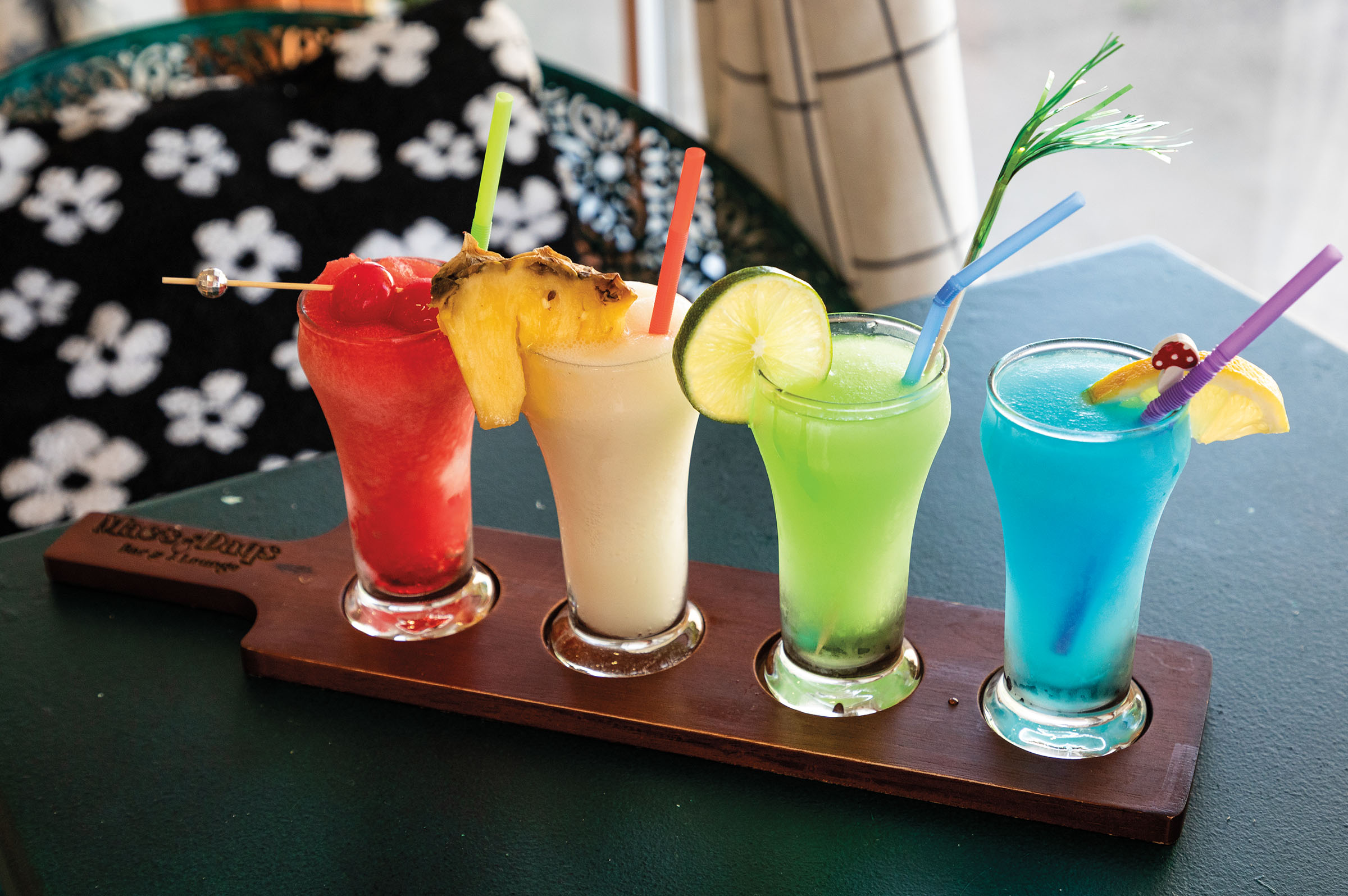 Four glasses of bright frozen drinks served on a wooden platter