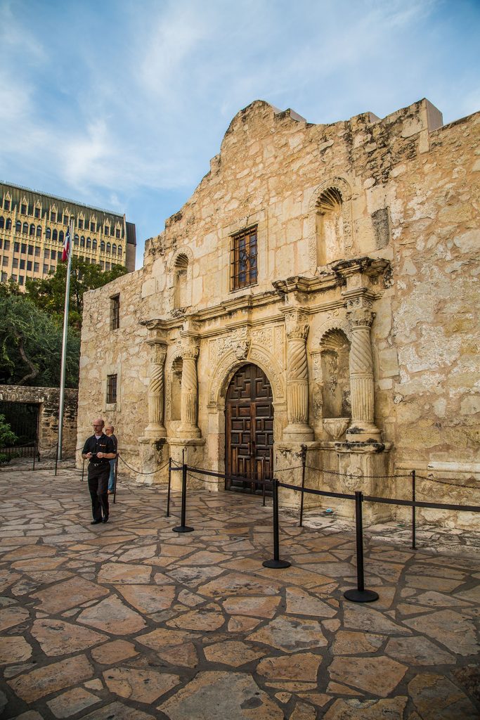 The stone exterior of The Alamo, with a tour guide speaking in front