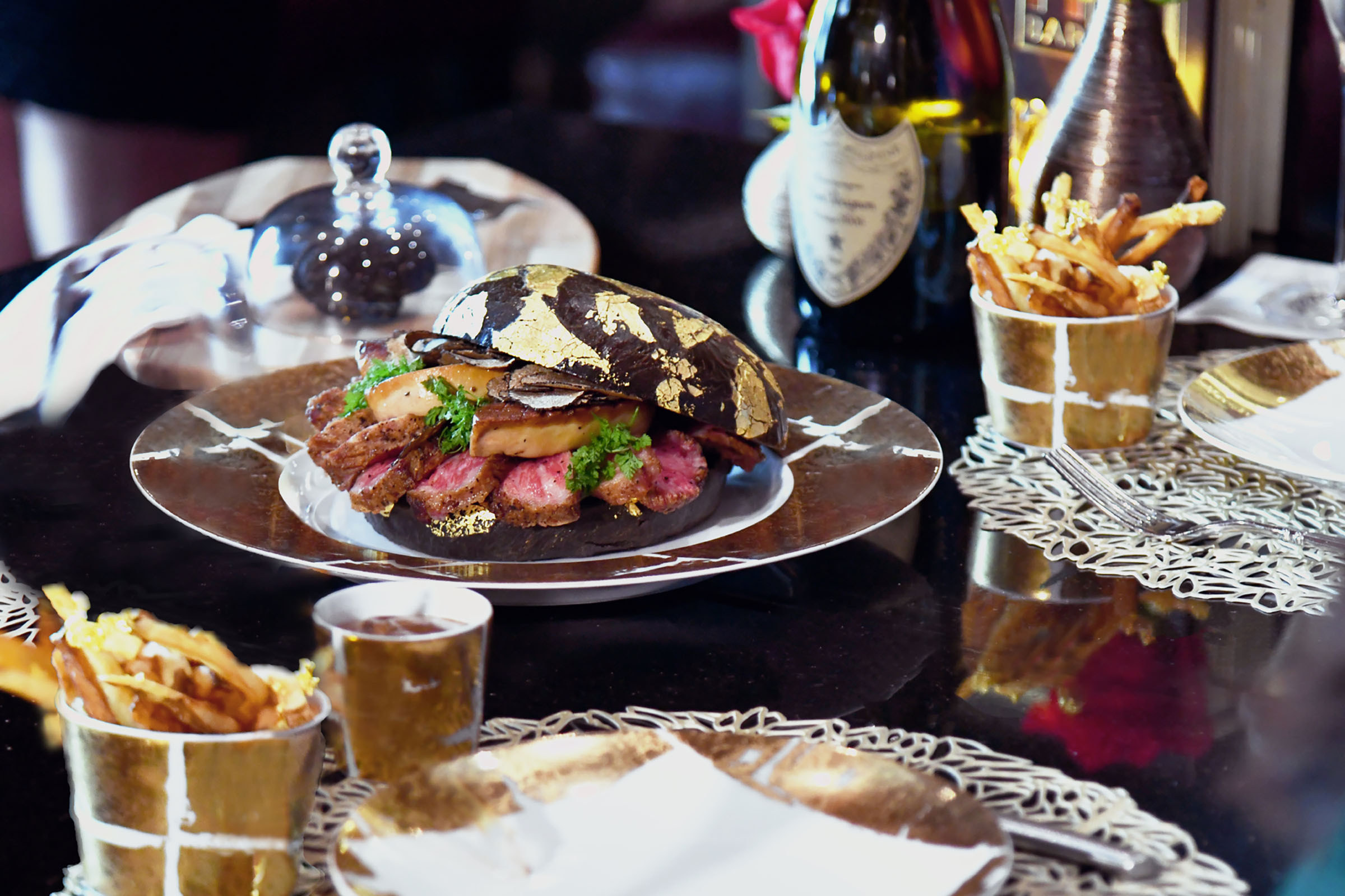 A gold leaf-crusted burger with a bottle of champagne and other luxurious sides