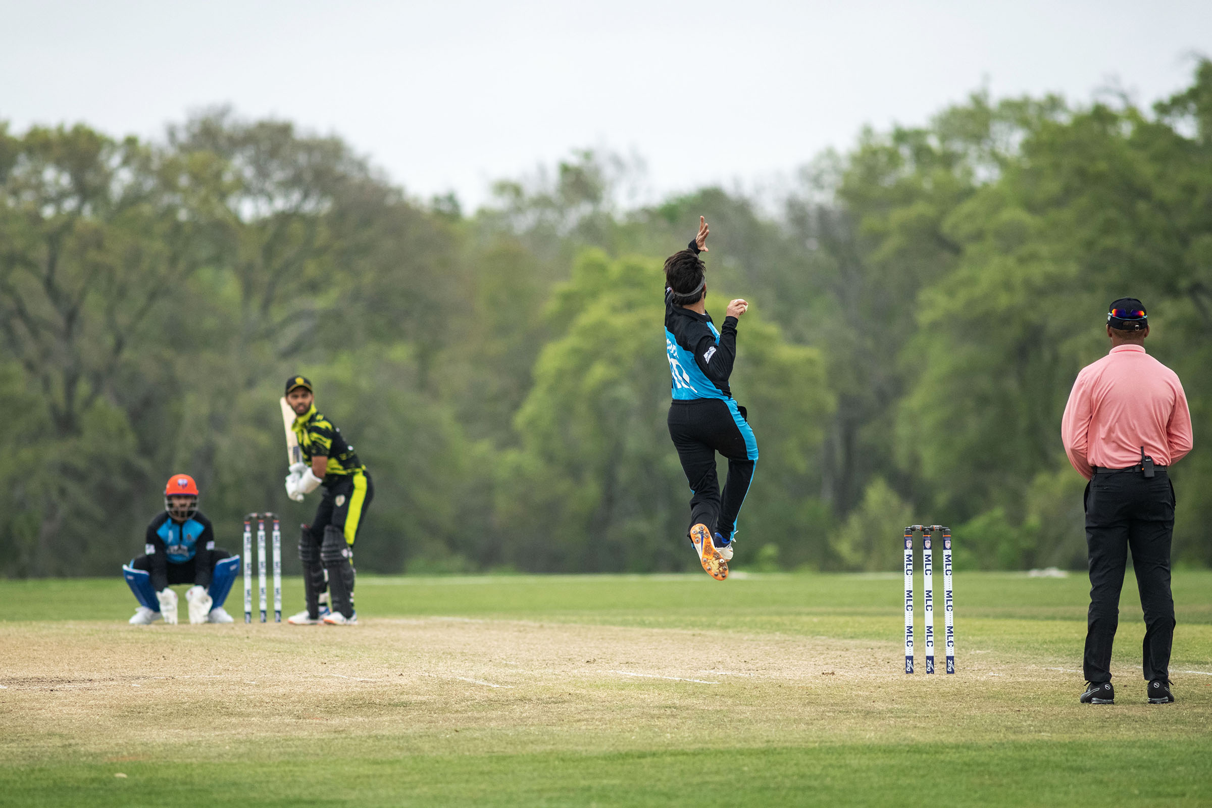 A cricket player jumps and throws a ball from one set of wickets down the field