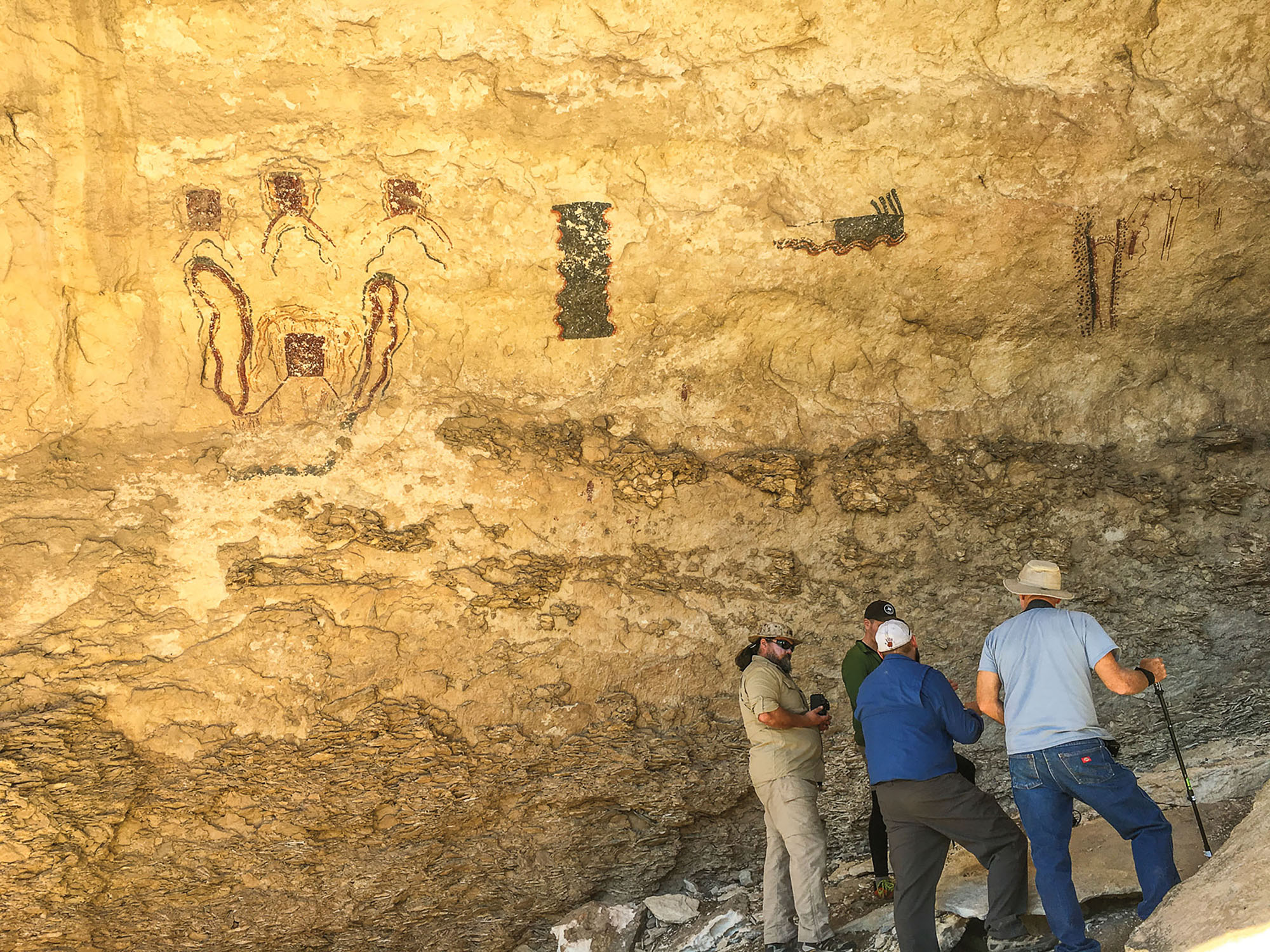A group of people look at dark cave paintings in a yellow-walled cave