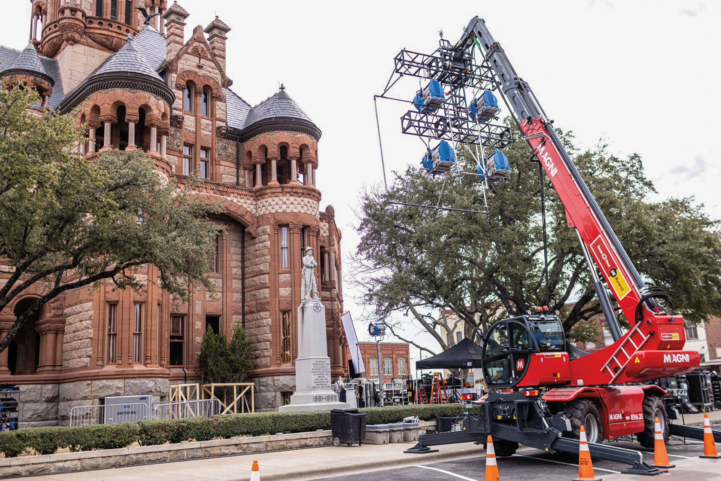 A large red boom truck moves filming equipment near an old brick courthouse