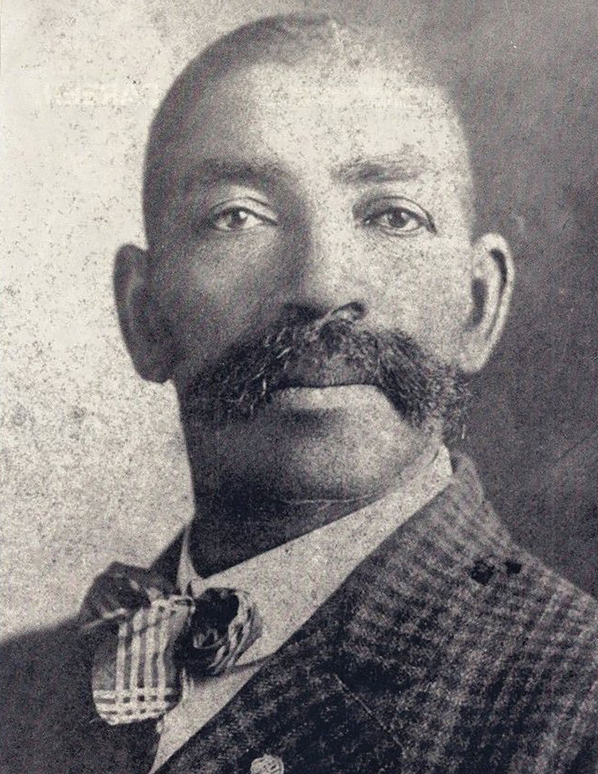 A historic photograph of a man wearing a checkered suit and bow tie