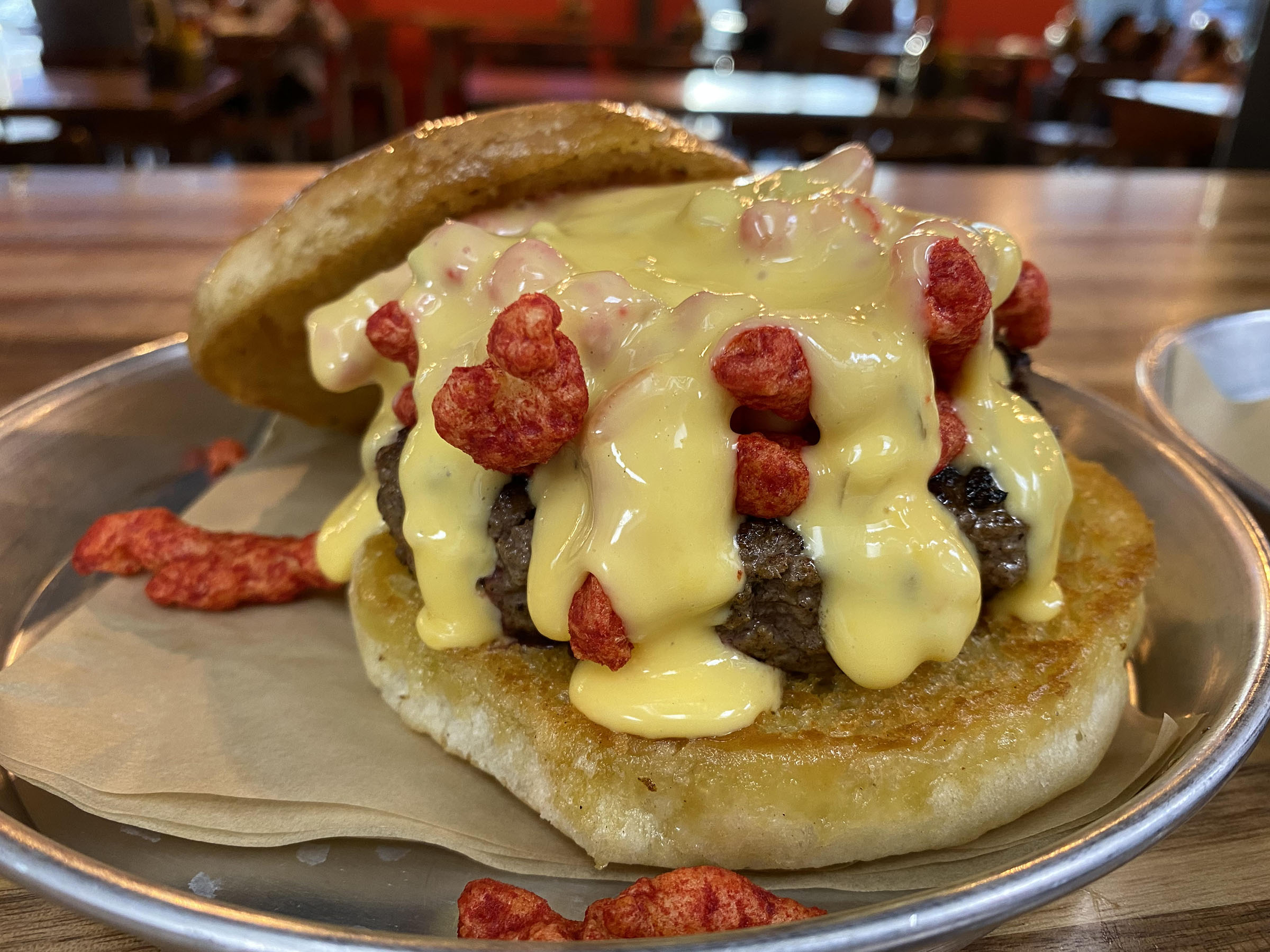 A burger patty piled high with meat, queso, and Flamin' Hot Cheetos