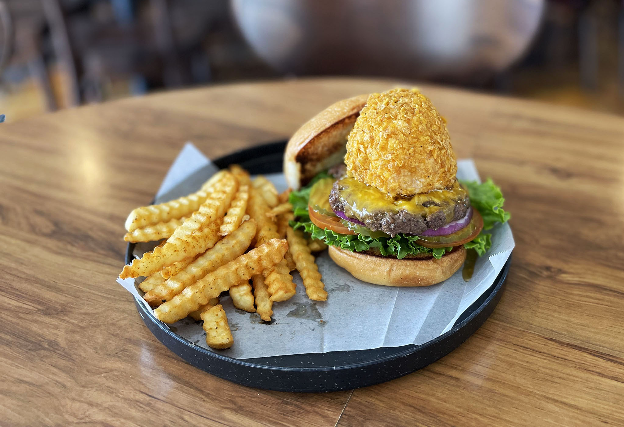 A burger and fries with the burger patty topped with a large scoop of fried ice cream