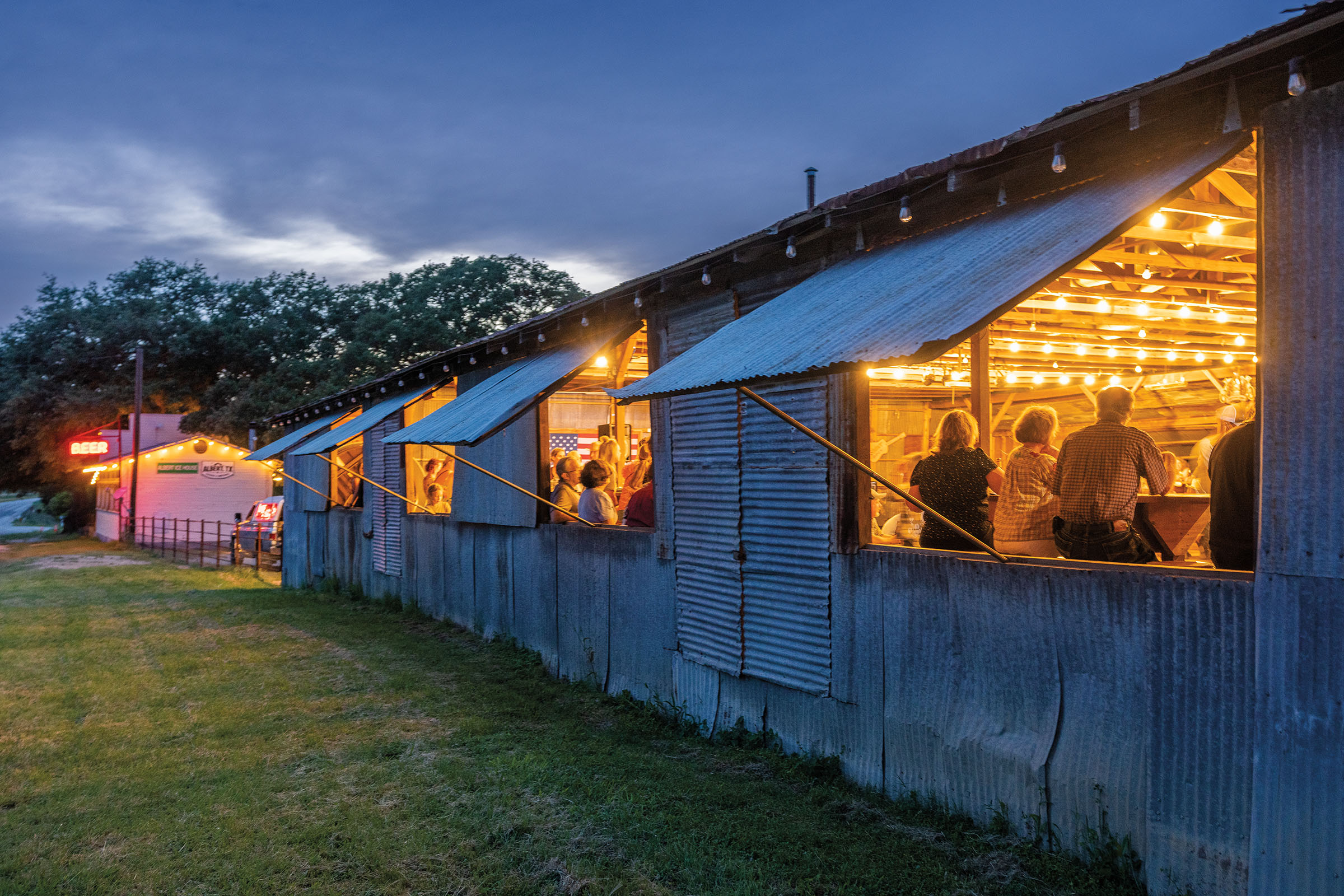 Bright yellow lights illuminate the windows of a metal-walled dancehall filled with people