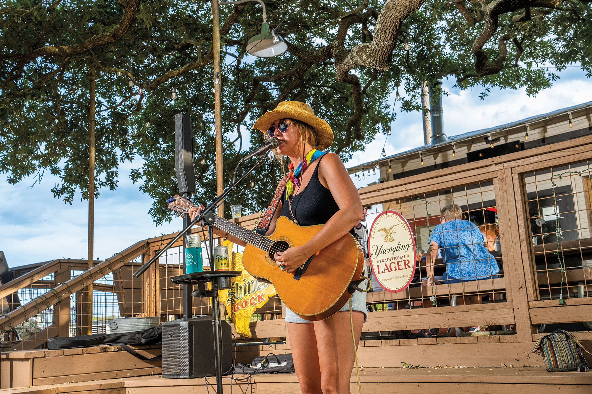 A woman wearing a cowboy hat plays an acoustic guitar on an outdoor stage