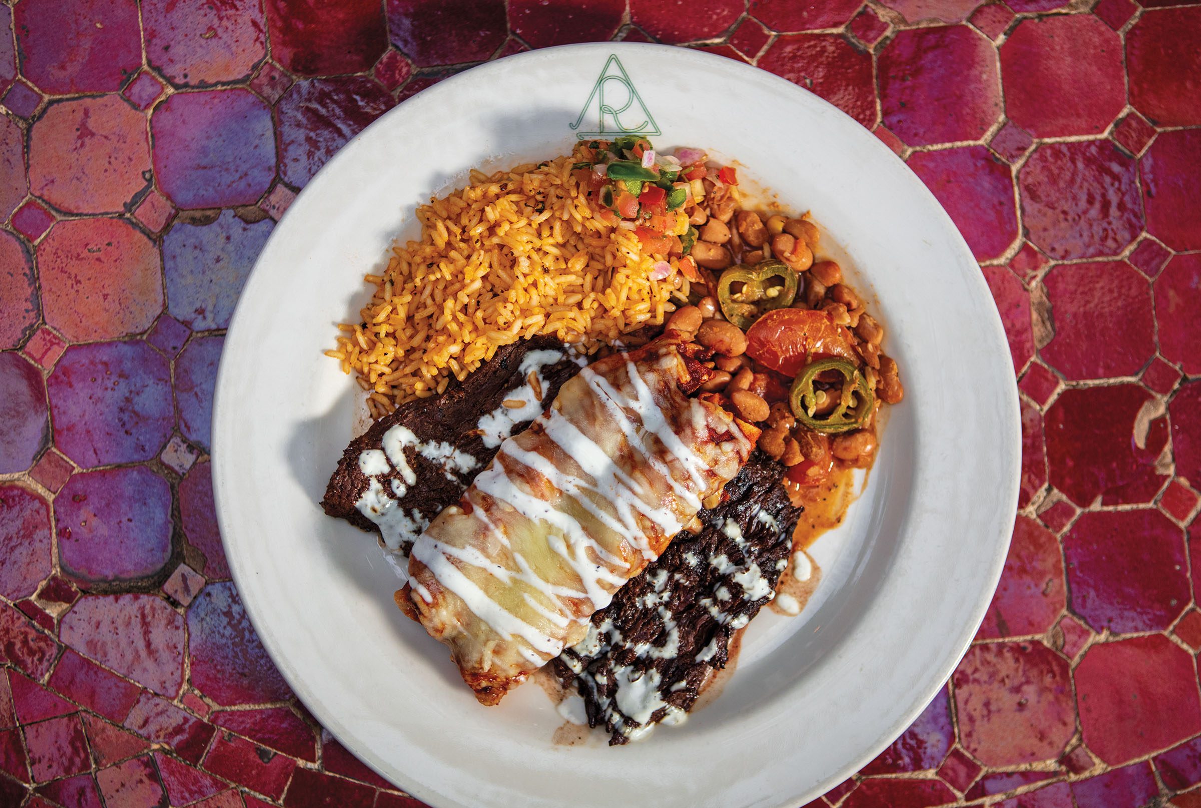 An overhead view of meat, enchilada, rice, and beans on a plate