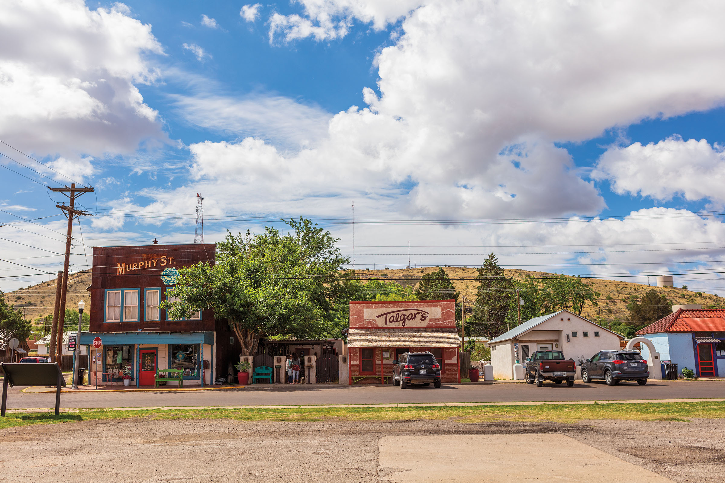 A collection of old buildings beneath a small brown mountain and blue sky